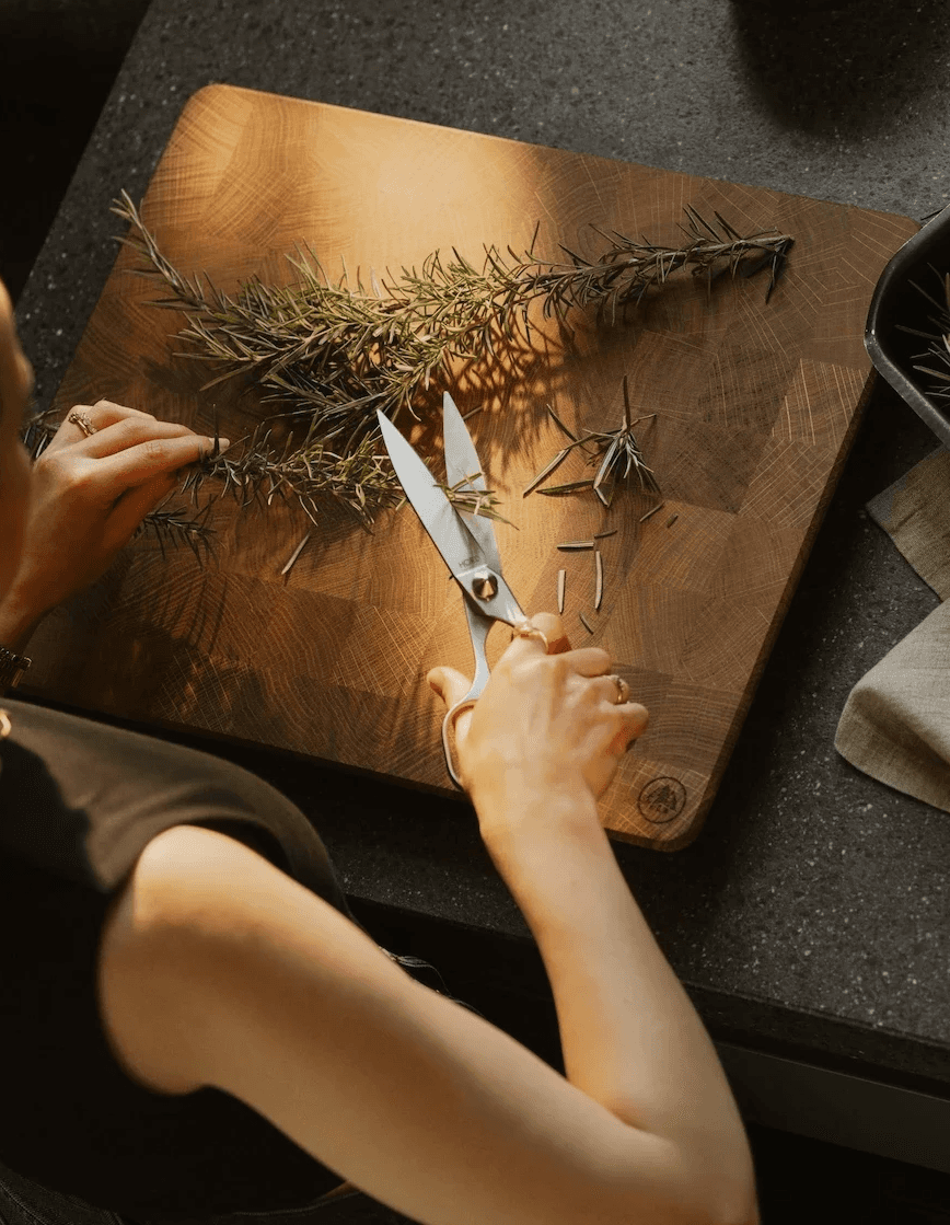 Close-up of a person using Horl stainless steel household scissors to cut fresh green herbs in a kitchen setting.