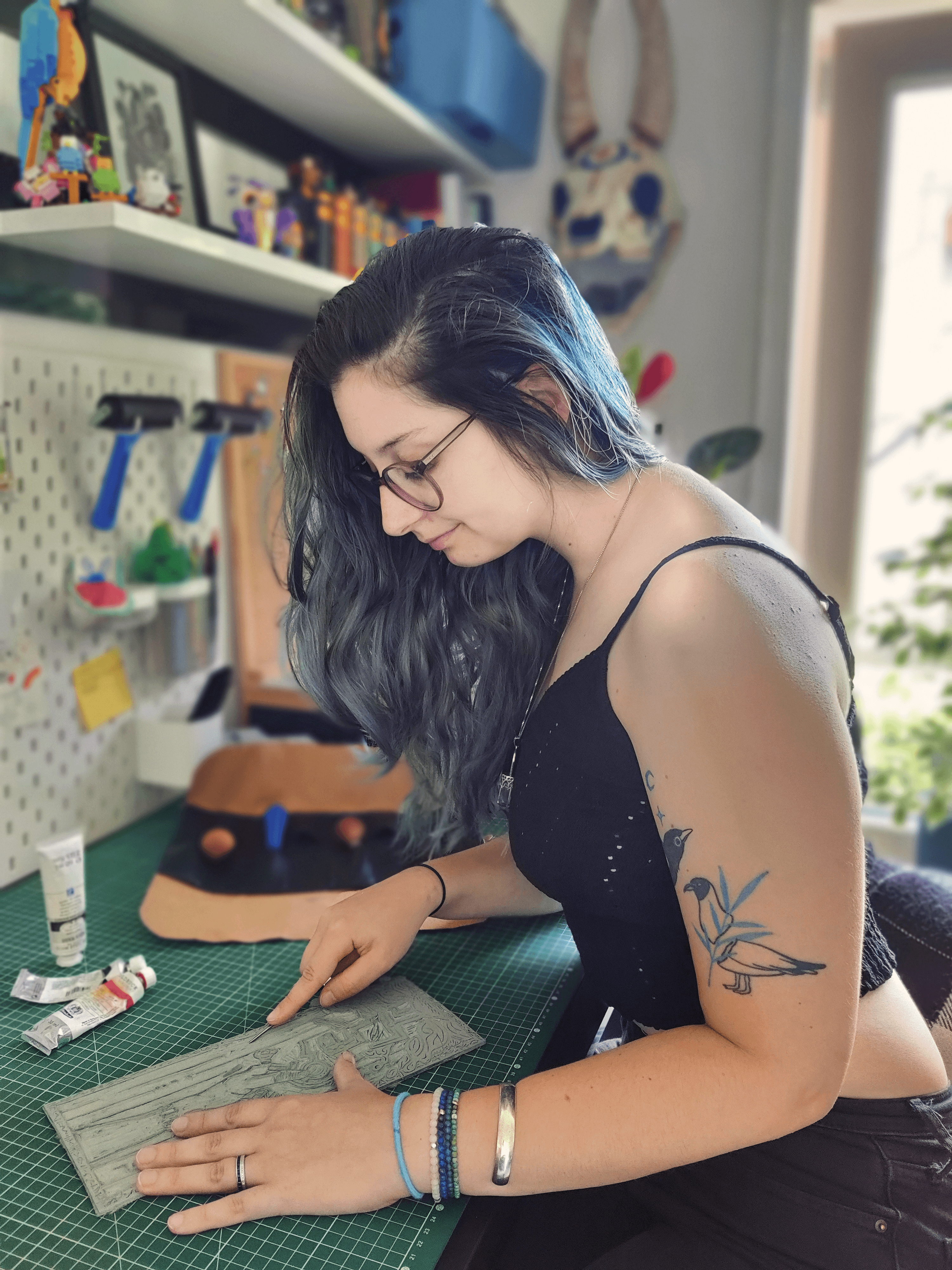 Un autre portrait de moi. Je suis dans mon atelier, en train de graver une plaque de lino avec une gouge. On voit mon matériel en fond (peinture, rouleau, gouges).