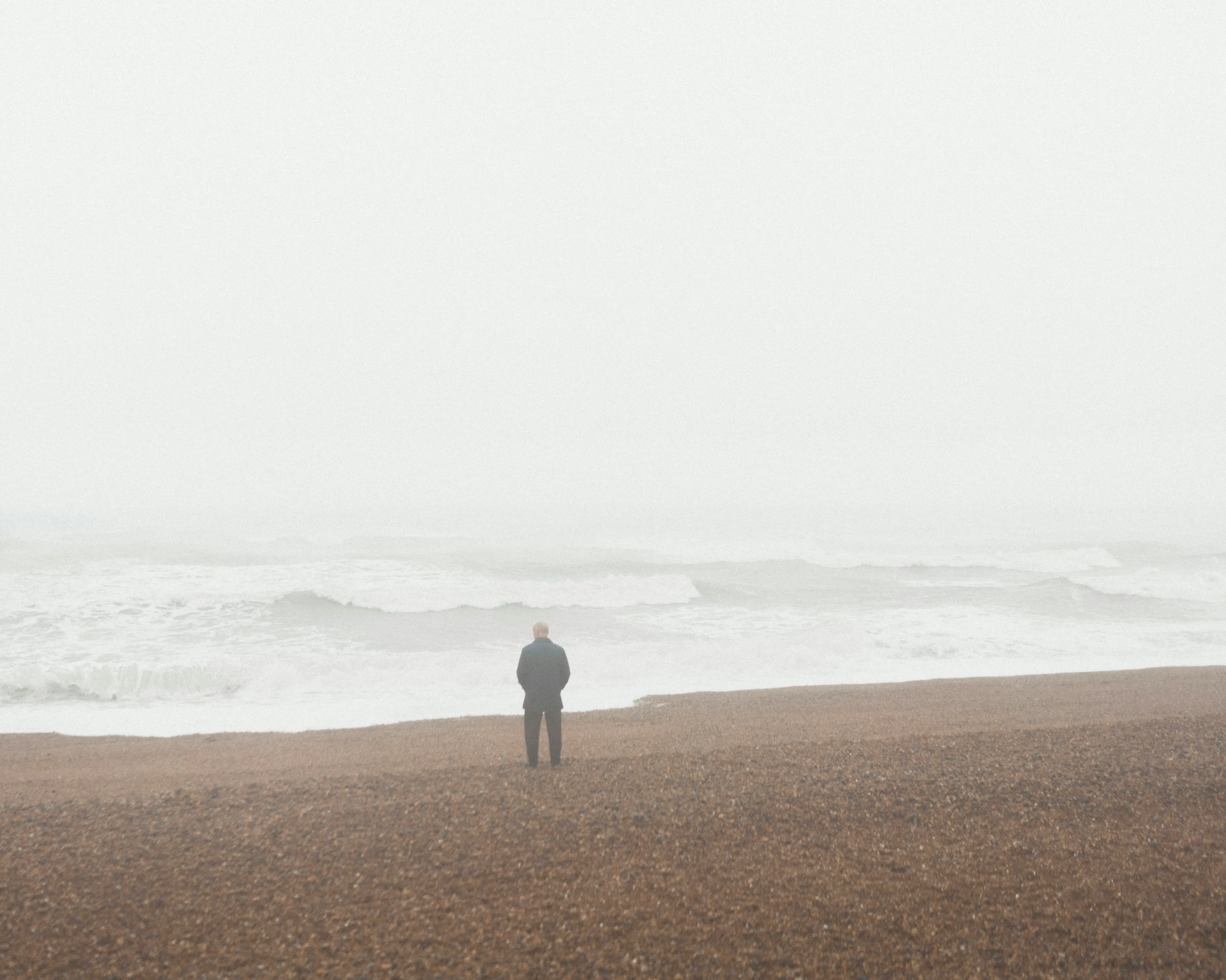 a lone figure stands on a foggy beach, with gentle waves lapping at the shore in the background