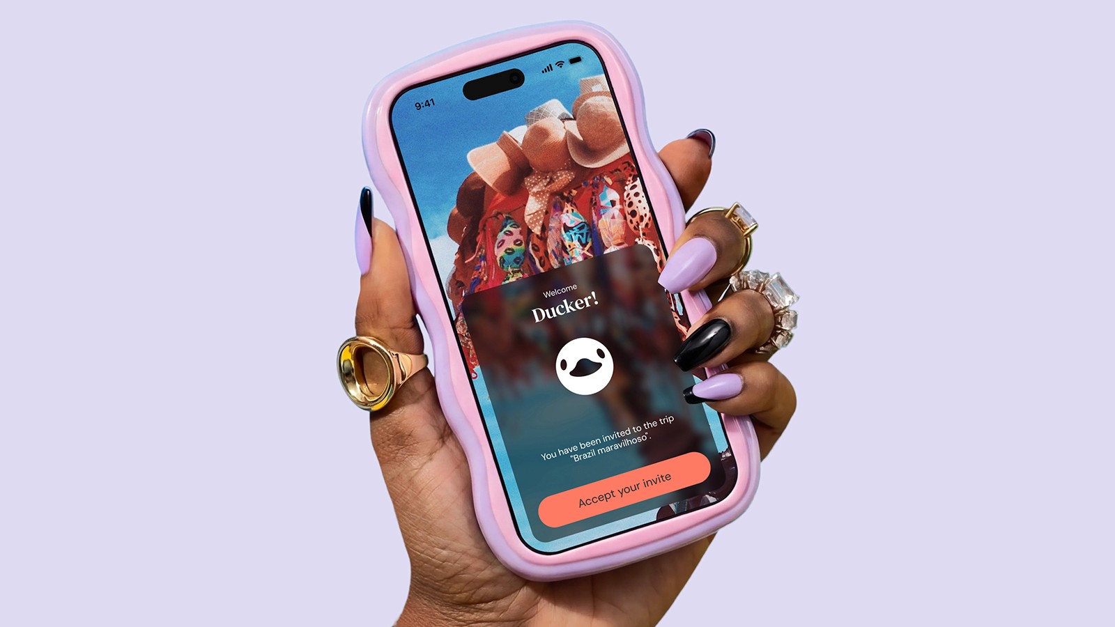 A hand with lilac and black manicured nails holding a smartphone in a wavy pink case. The screen displays a "Welcome Ducker!" invite from DuckAround notification over a travel-themed background.