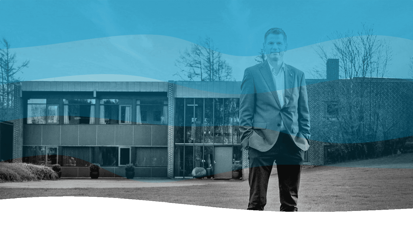 Een man in een pak en stropdas staat met zijn handen in zijn zakken voor een gebouw. Blauwe golven als overlay zorgen voor rust en professionaliteit.