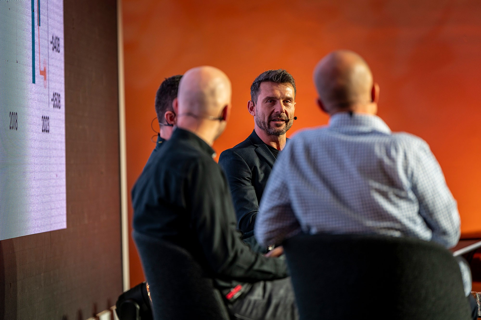 Panel discussion at Money Maker conference by CzechCrunch in Prague, speaker addressing audience on stage with branded backdrop and warm lighting