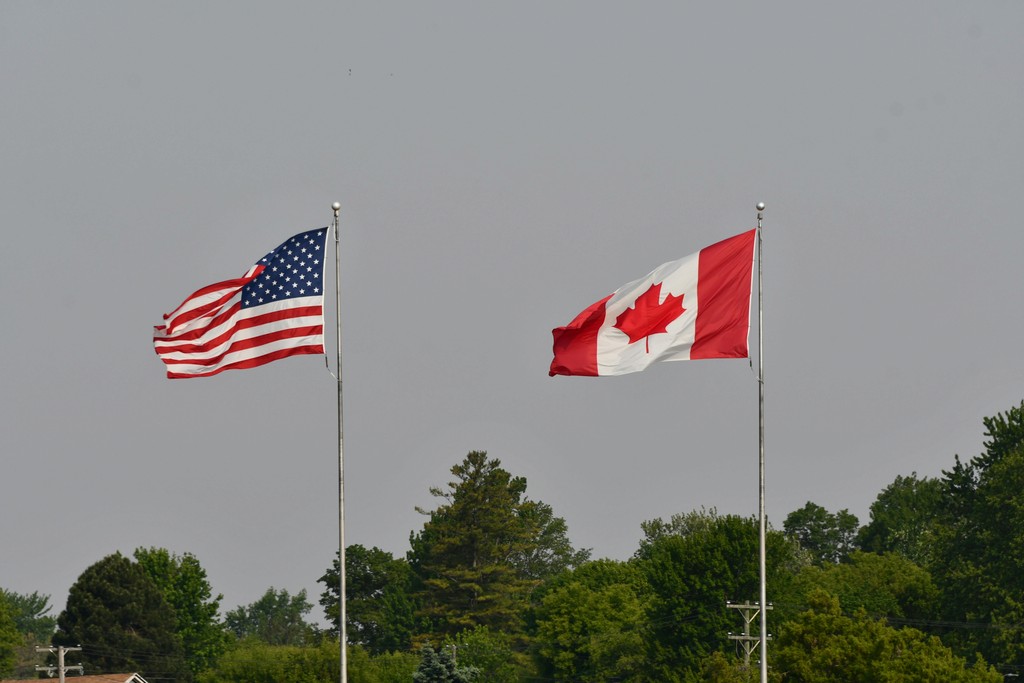 The United States and Canadian flags flying side-by-side outdoors, representing the integrated North American border, new 2026 dual citizenship updates, and CUSMA work visa options for US citizens relocating to work in Canada.