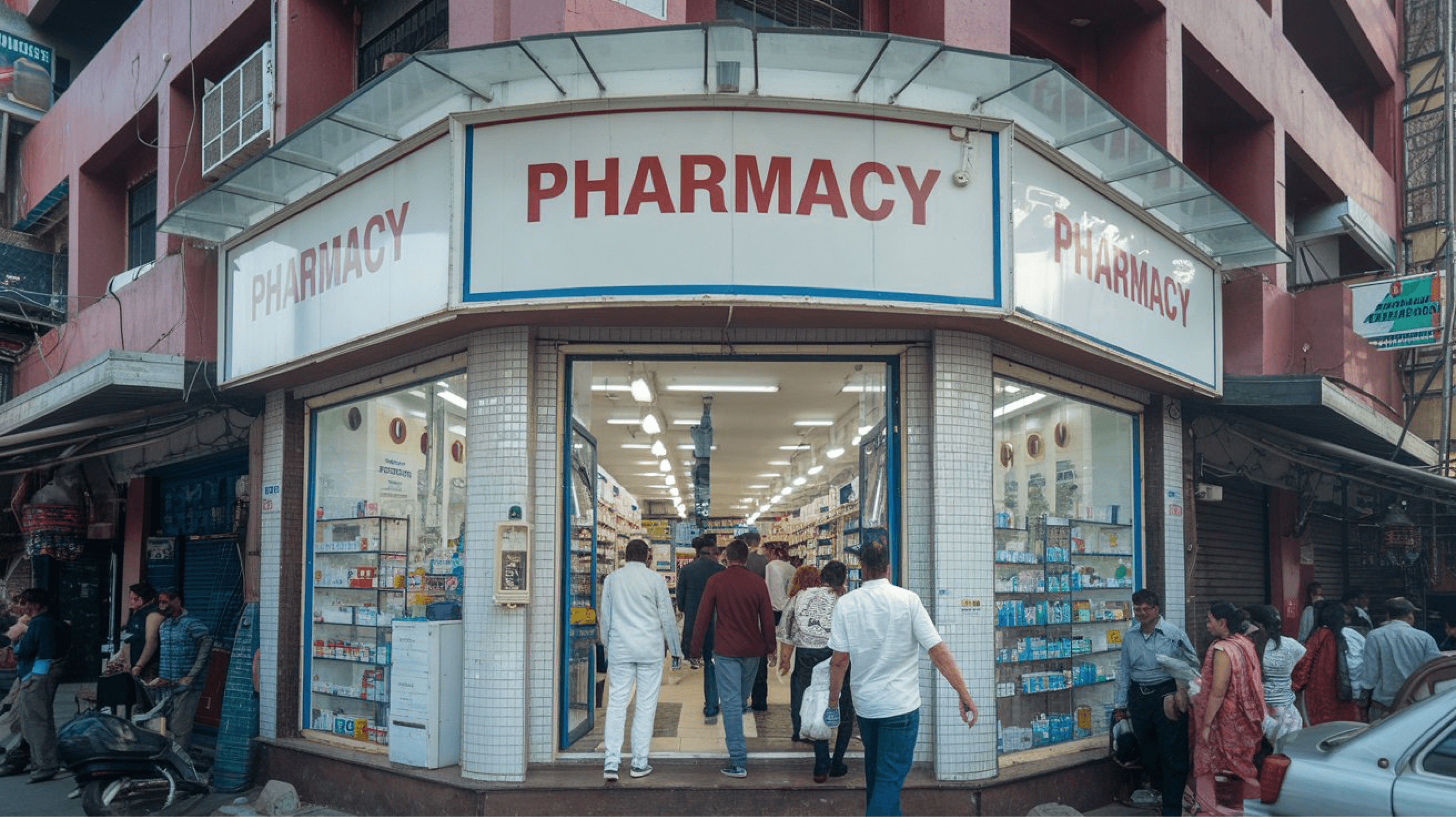 Street-level view of a pharmacy located in a busy urban area with a bright, clean facade and a clear sign reading 'PHARMACY.' The store entrance is bustling with customers entering and exiting, reflecting high footfall and the availability of a wide range of pharmaceutical products. This highlights the accessibility and trust customers place in their neighborhood pharmacies. Pharmacy Startup Guide, How to Open a Pharmacy in India, Pharmacy Management Software, GST Compliant Pharmacy Billing, Pharmacy Business Tips, Inventory Management for Pharmacies, Step-by-Step Guide for Pharmacy Owners, Pharmacy Setup India, Digital Pharmacy Tools, Pharmacy Operations in India, Beginner’s Guide to Pharmacy Business, Streamline Pharmacy Management, Pharmacy Billing Solutions, Pharmacy Software India, Pharmacy Pro Solutions