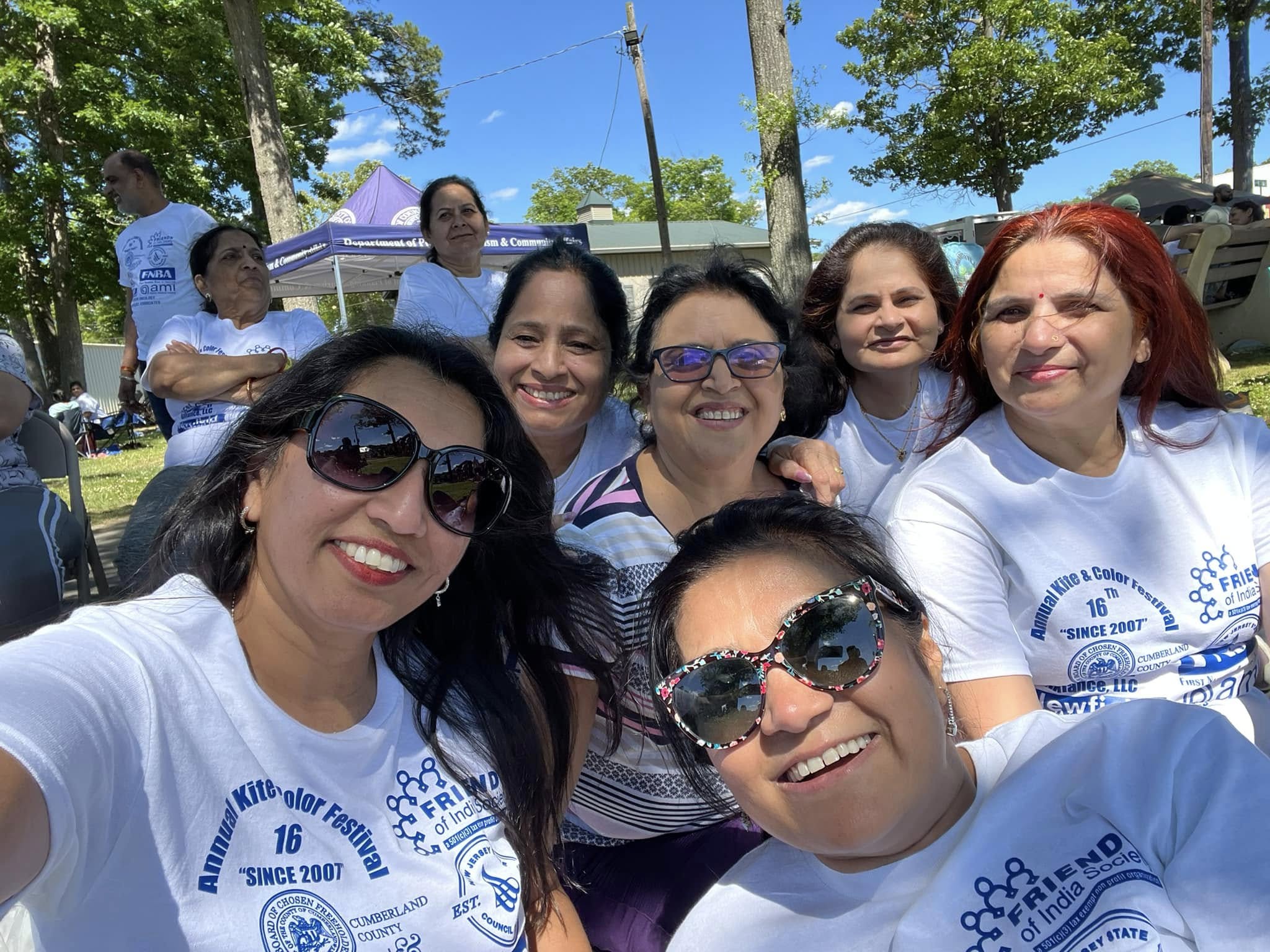 A woman wearing a purple sweater holds a green smartphone and smiles warmly under a clear blue sky, conveying happiness and connectivity.