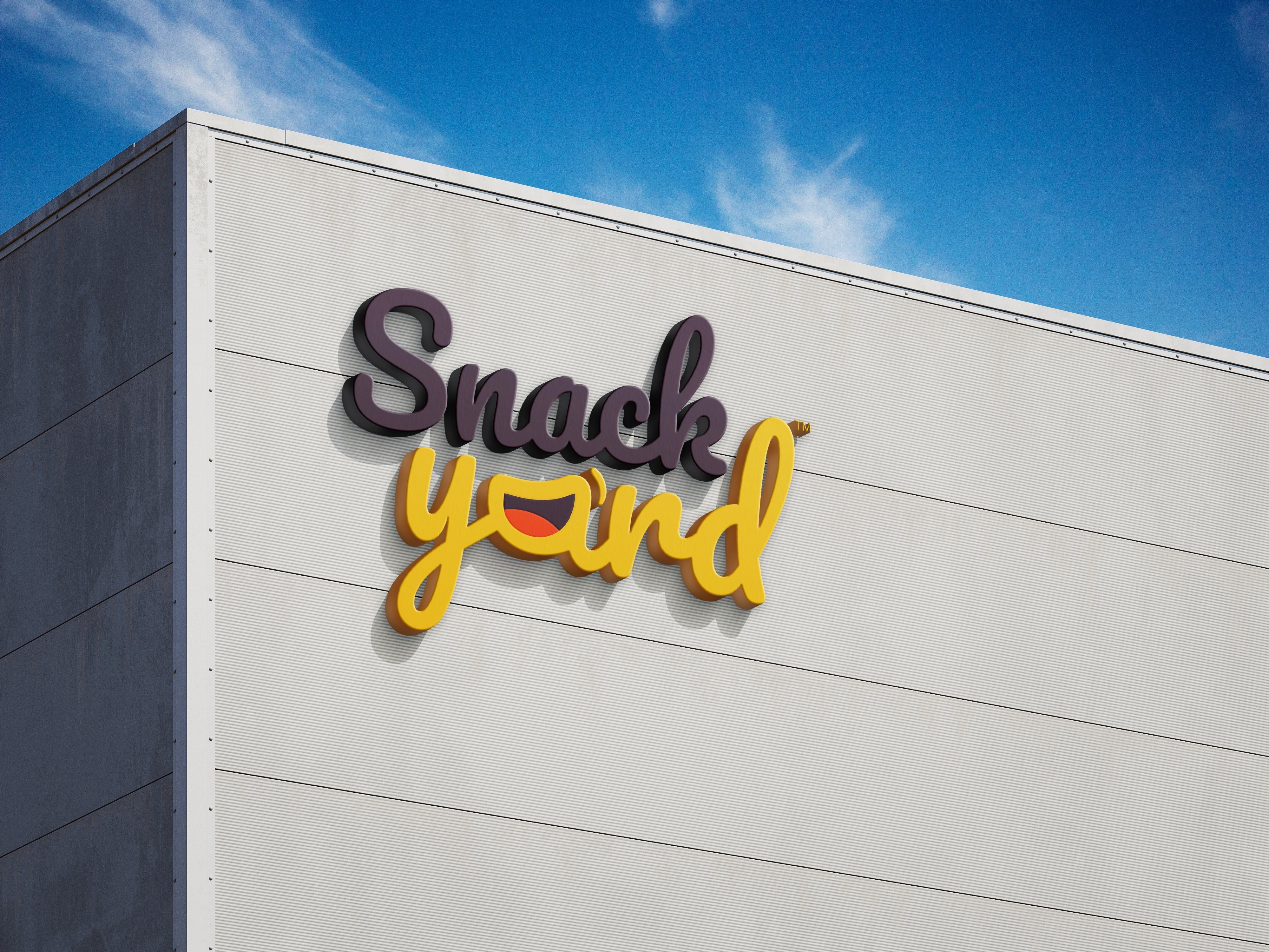 Side-by-side graphic featuring a dark panel with the headline “We bring global snacks and drinks to Saudi — and keep them selling,” supporting text about helping brands enter and grow in KSA, and a yellow button labeled “Why Work With Snack Yard.” On the right, a building exterior displays a large “Snack Yard” logo in bold black and yellow lettering against a blue sky.