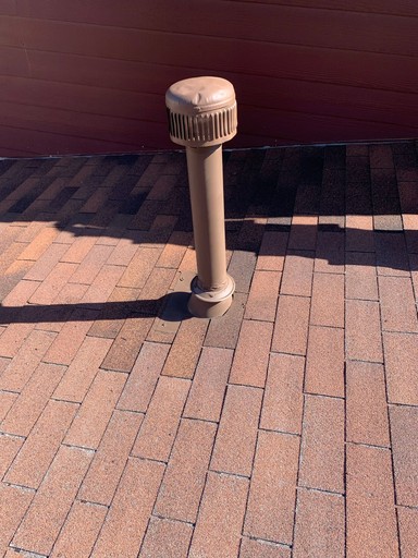 Roof detail: a tall capped vent and its flashing beside the wall, surrounded by the repaired architectural shingle courses.