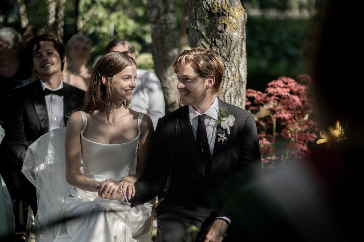 Bride in a satin dress and groom in a black suit smiling at each other during a garden ceremony