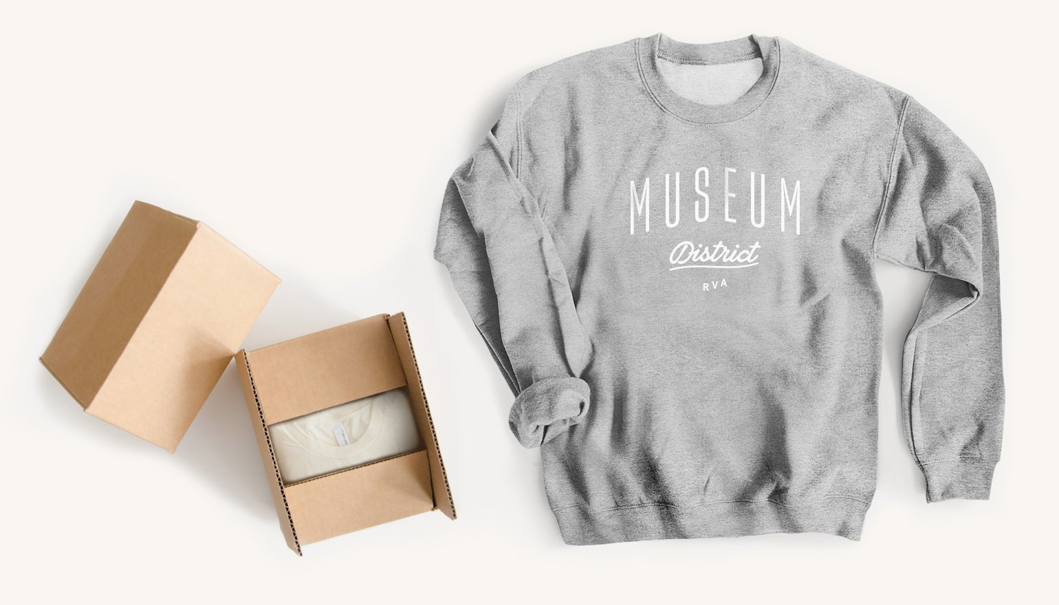 Gray Museum District sweatshirt next to cardboard boxes with folded t-shirt.