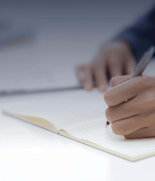 A close-up of hands holding a pen, writing on a sheet of paper.