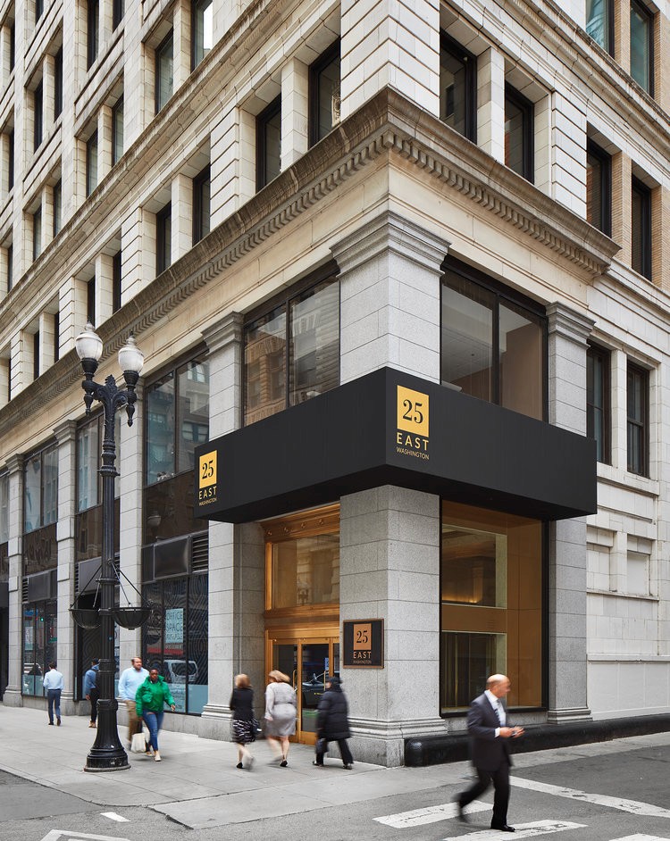 Exterior of TMBR’s office at 25 East Washington Street in Chicago, featuring a modern black awning with gold signage, large windows, and a historic architectural facade.