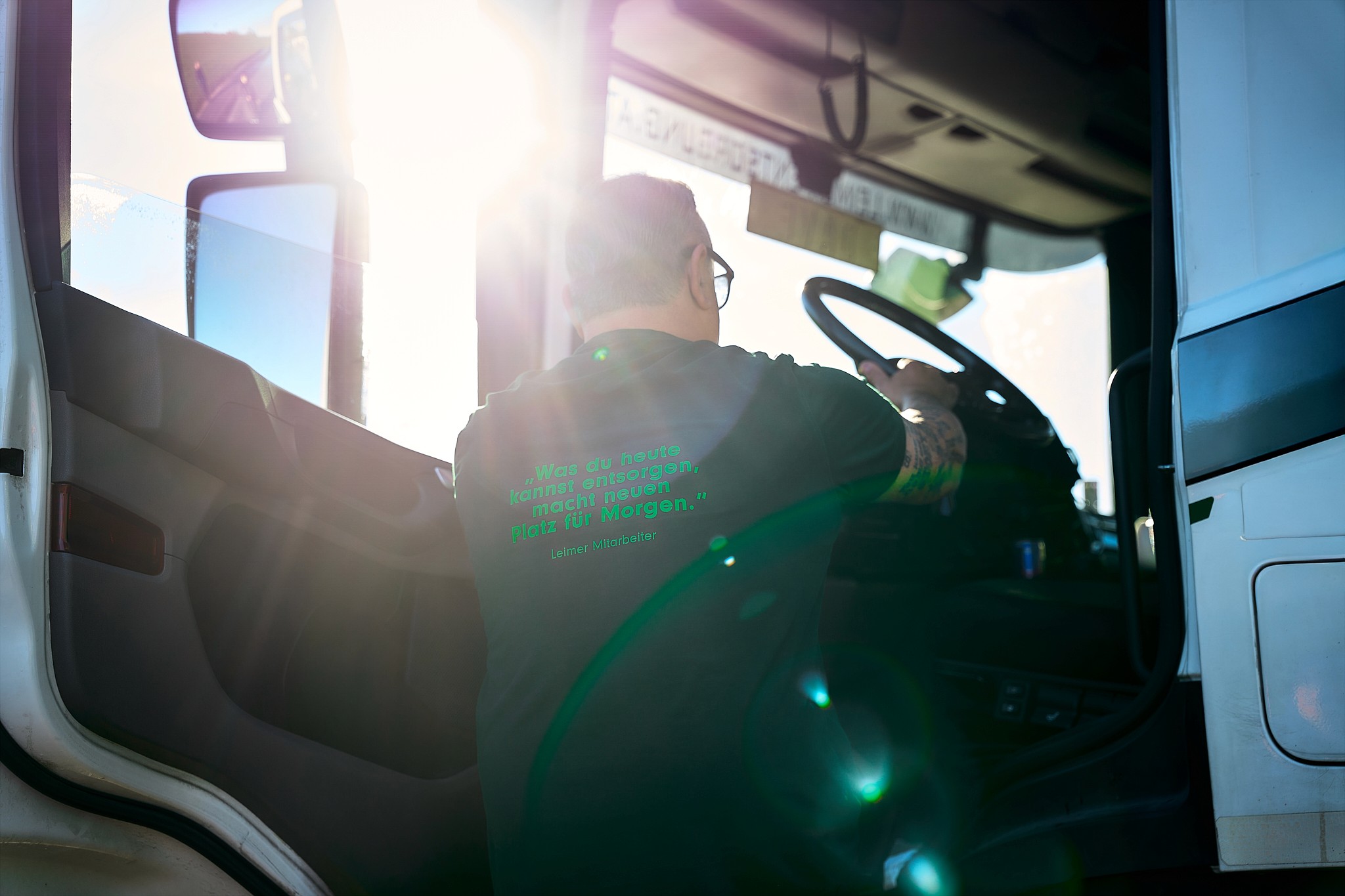 LKW-Fahrer sitzt am Steuer. Mann in Brille und grünem Shirt bei der Arbeit im Führerhaus eines Lastwagens.