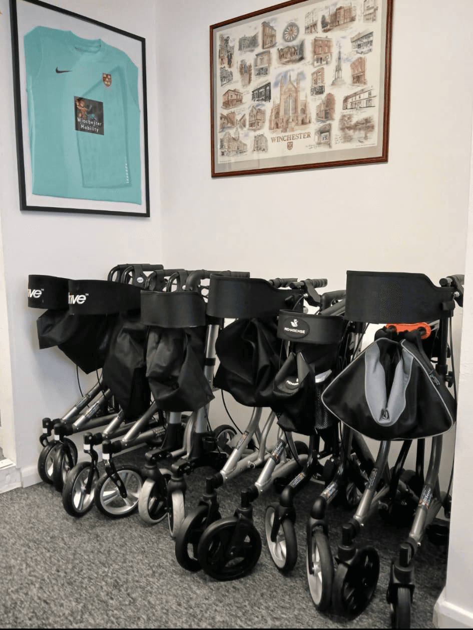 image shows a range of rise and recliner chairs in the backgroud. In the foreground is a rage of 3 and 4 wheeled walkers also known as rollators. 