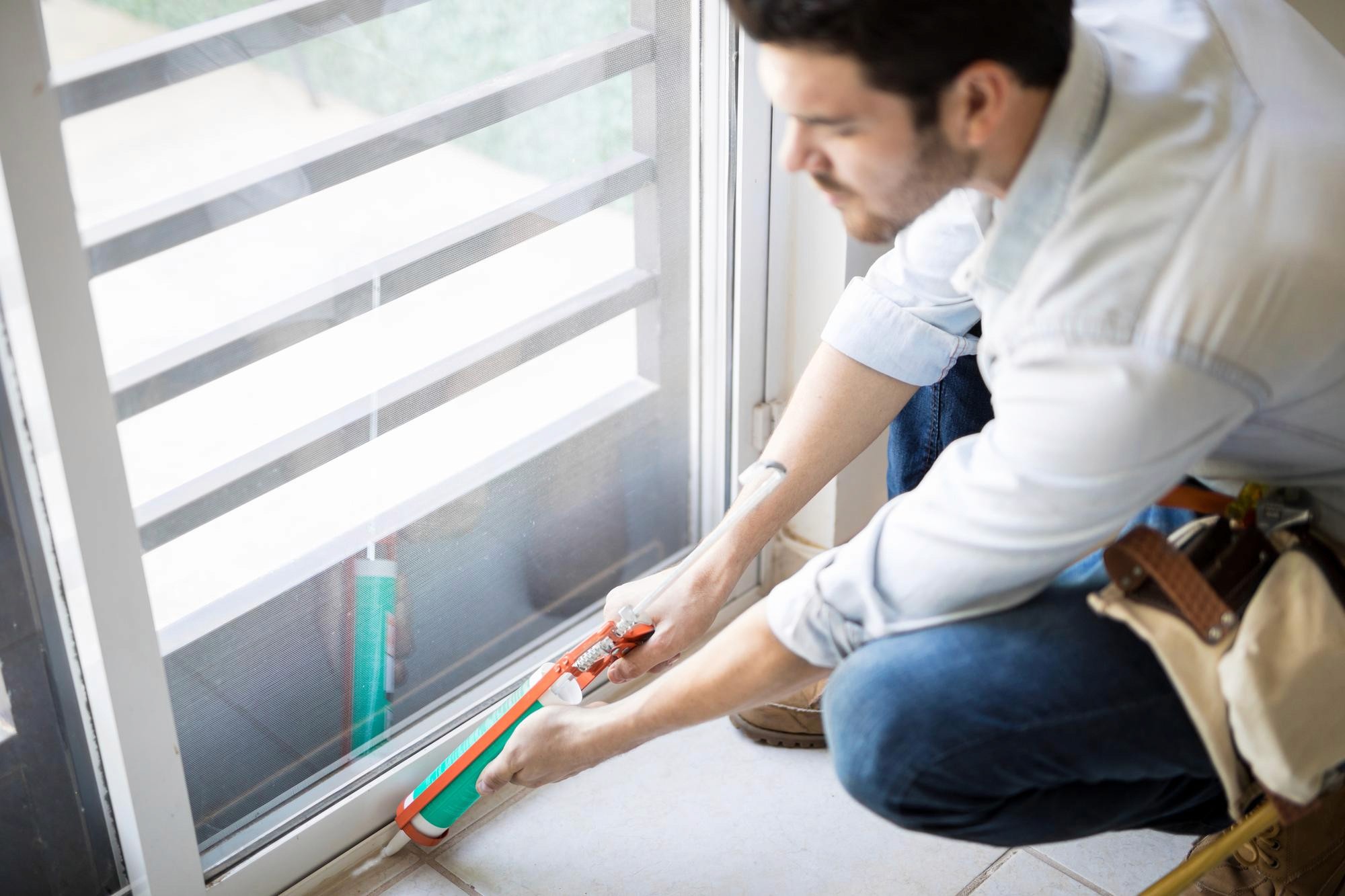 A homeowner sealing a window frame with weatherstripping.