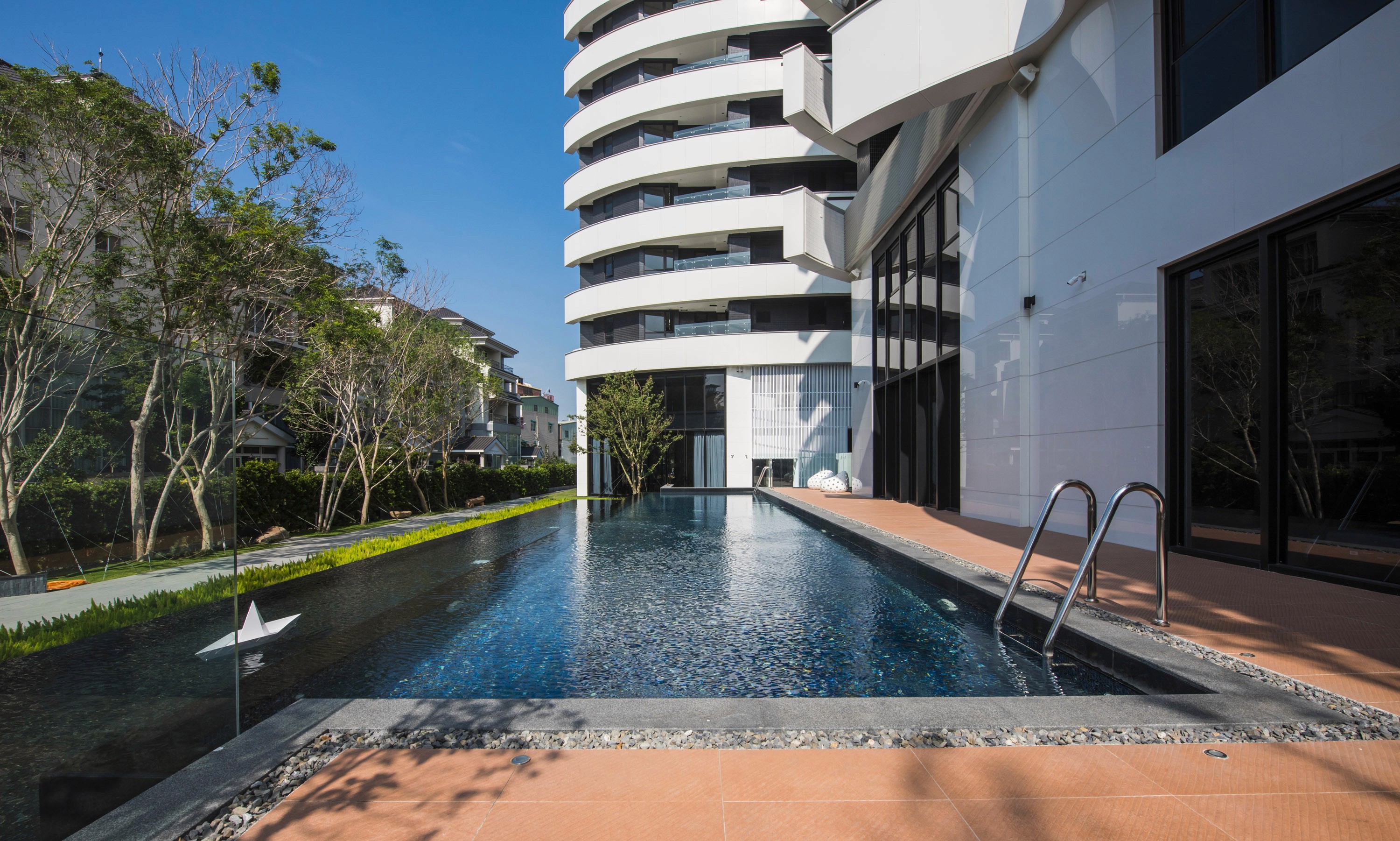 Curving residence exterior with pool and landscape, daytime.
