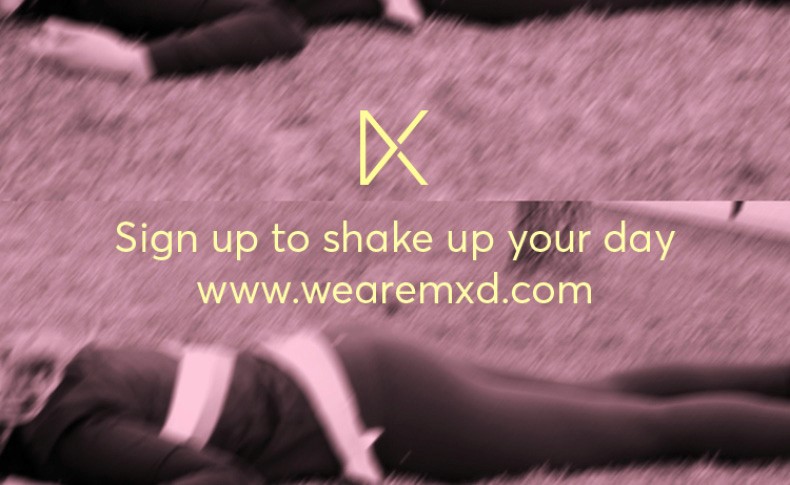 The image is split into two sections. The top section features a stylized yellow "X" logo against a blurred purple background. Below it, the text “Sign up to shake up your day” is displayed in yellow, followed by the website address “www.wearemxd.com” in white. The bottom section shows a blurred image of a person lying down on a purple surface. The image is monochromatic, with no additional colors or patterns.