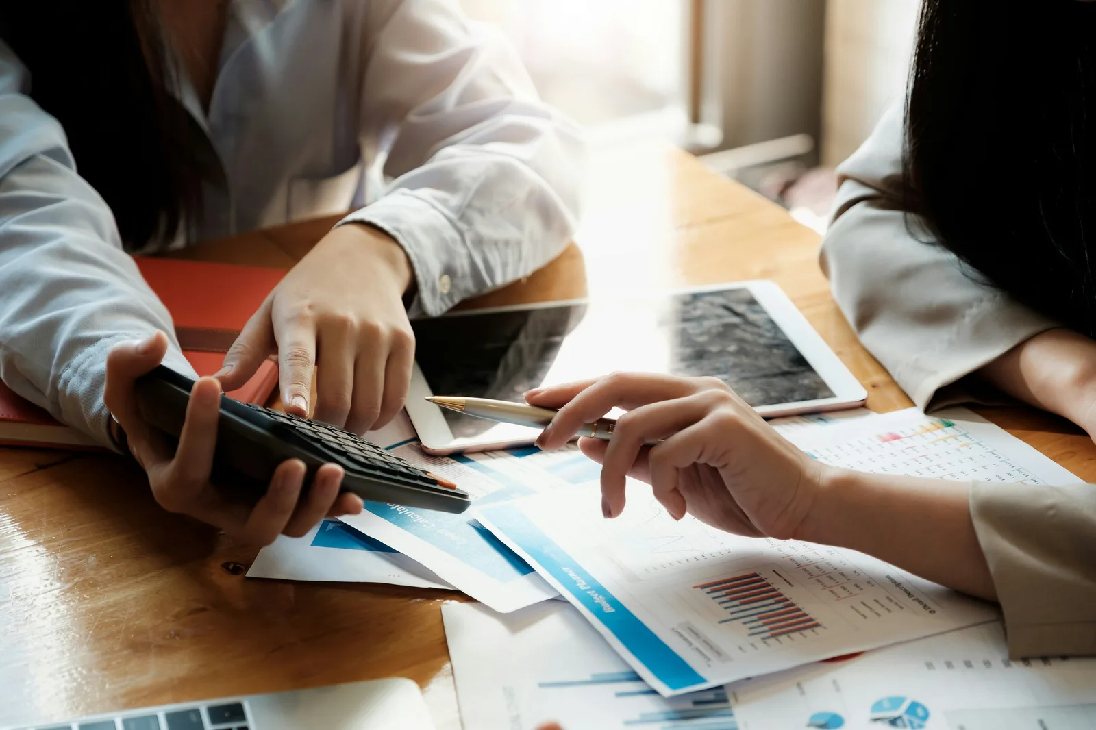 Двама души анализират финансови графики с калкулатор на бюро