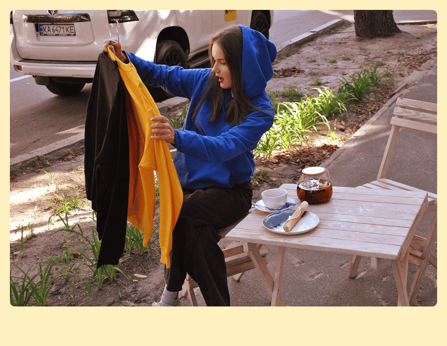 дівчина сидить, тримає у руках світшоти і дивується якісними принтами на світшотах