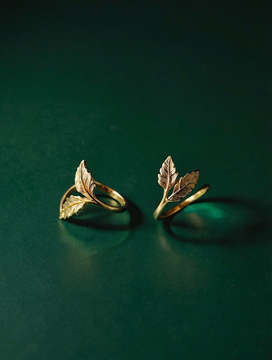 Elegant gold rings with intricate leaf designs on a deep green background, showcasing luxury and craftsmanship in a minimalist setting.