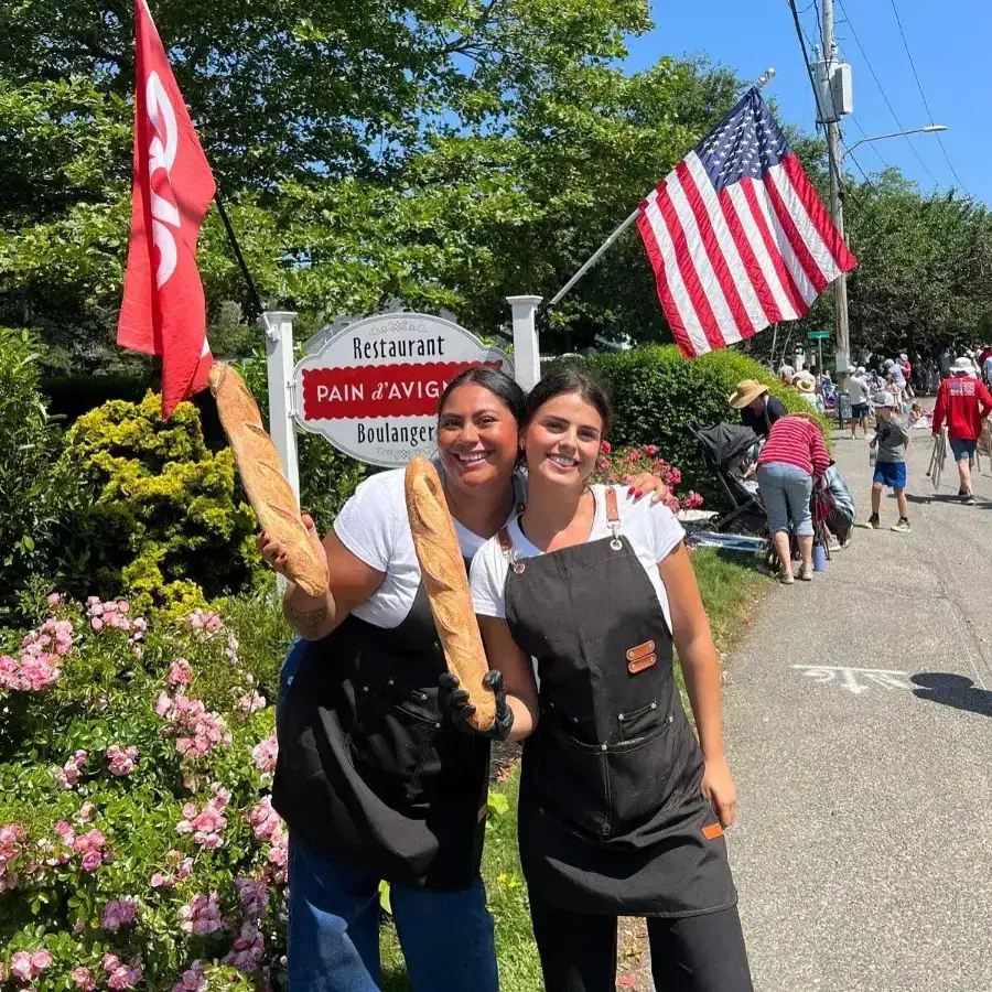 Two staff members smiling outside Pain D’Avignon during a festive community event with American flags at Chatham.