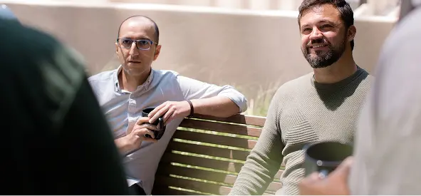 Two coworkers sitting outdoors at Cogent, holding coffee cups and talking during a casual team break.