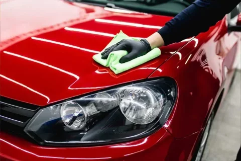 Hand polishing a red car with a microfiber cloth.