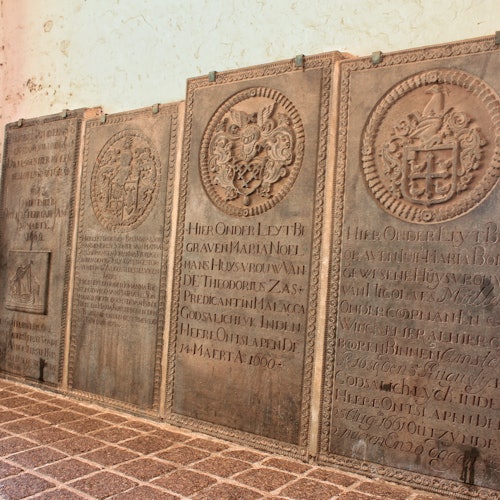 A row of engraved stone tablets with crests and inscriptions in a historic setting with a tiled floor.