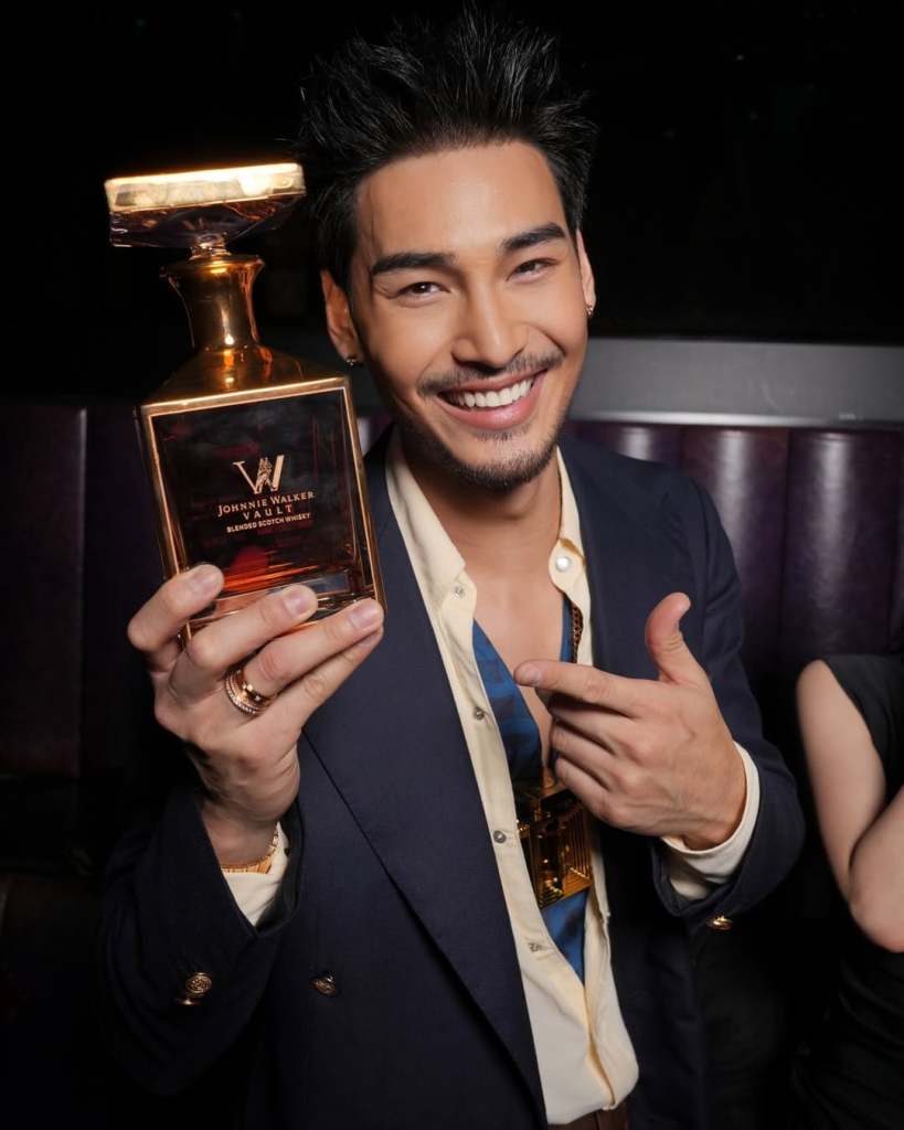A smiling man in a stylish outfit holds a golden Johnnie Walker Vault decanter, showcasing the collaboration with Olivier Rousteing.