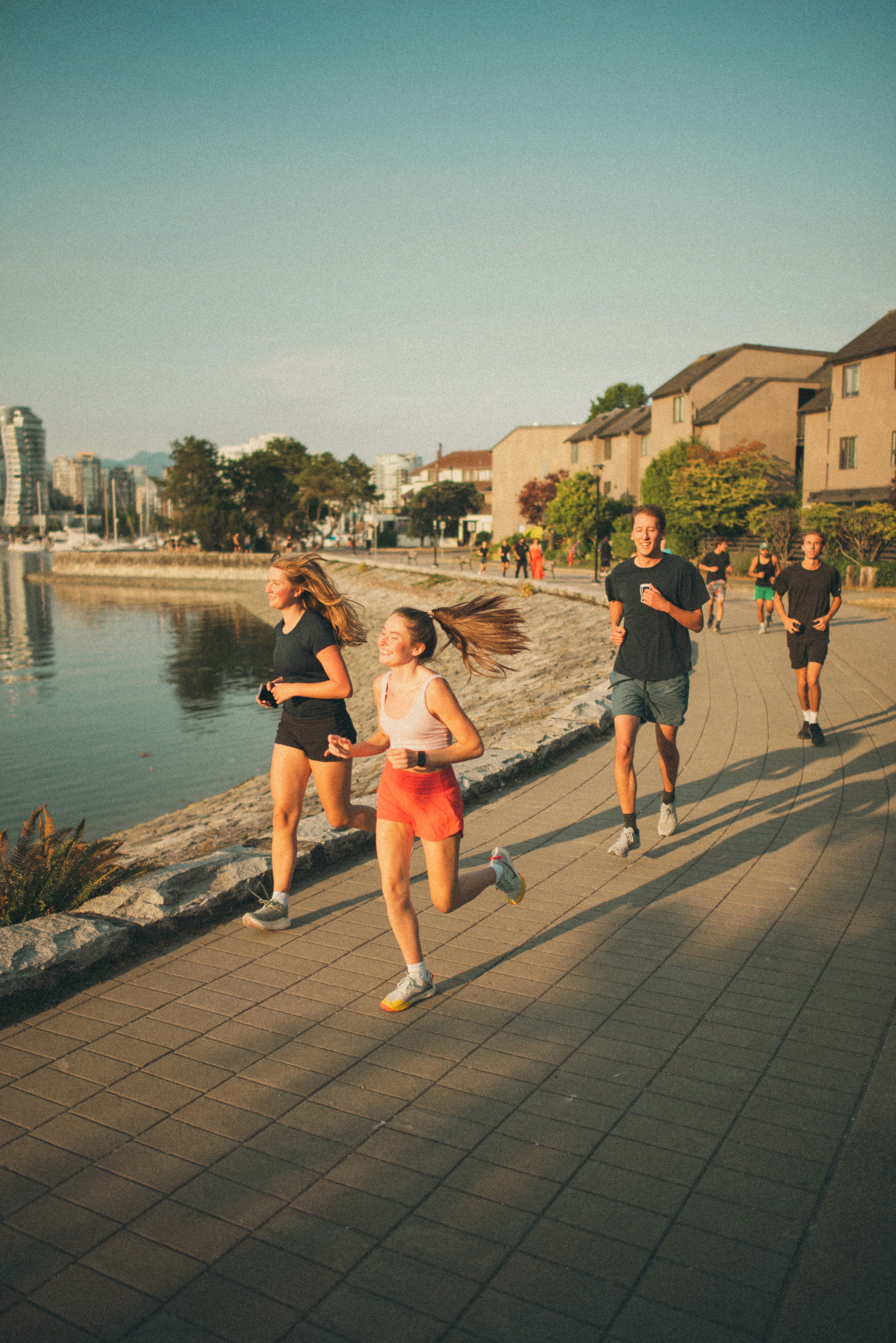 Athlete in a red tank top and black shorts sprinting outdoors, wearing white and red sports sunglasses under a clear blue sky.