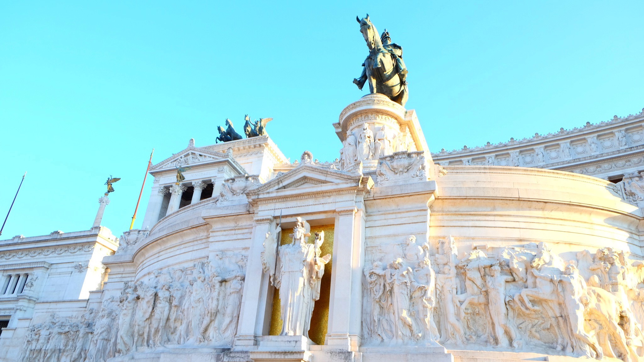 A couple stands on a sandy hill at sunset, facing away, with arms raised in a relaxed "hang loose" gesture. The scene conveys tranquility and joy.