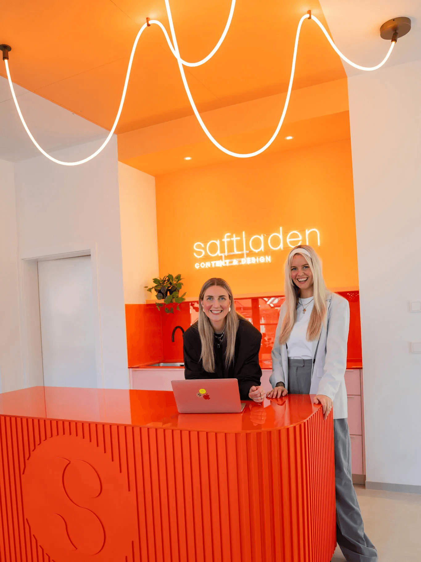 Zwei Frauen im Saftladen. Innenarchitektur mit orangefarbenem Tresen und Neonlicht. Saftbar