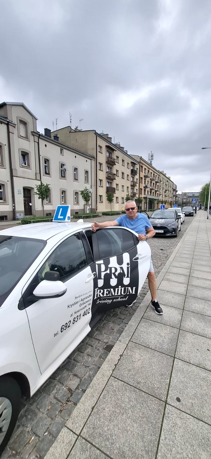Wiesiu Korczak – Instruktor oparty o biały samochód nauki jazdy Premium na tle miejskiej ulicy.