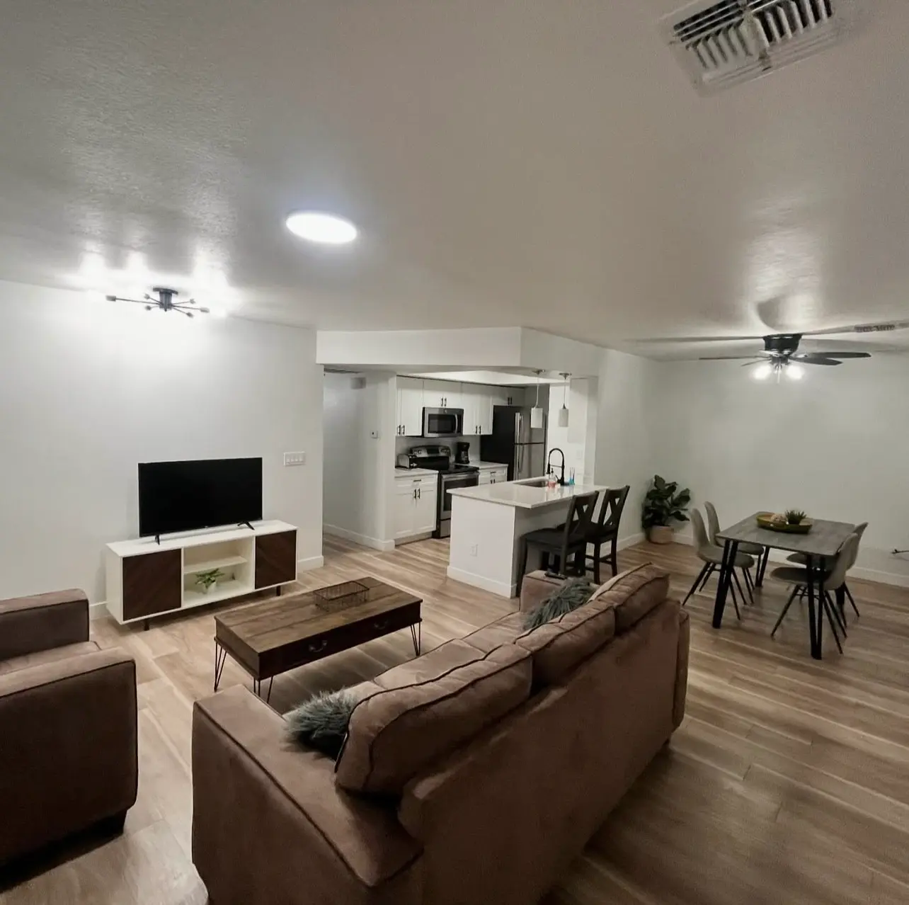 Professionally staged and cleaned Airbnb living room featuring a sanitized kitchen, dust-free ceiling fans, and vacuumed/mopped hardwood flooring.