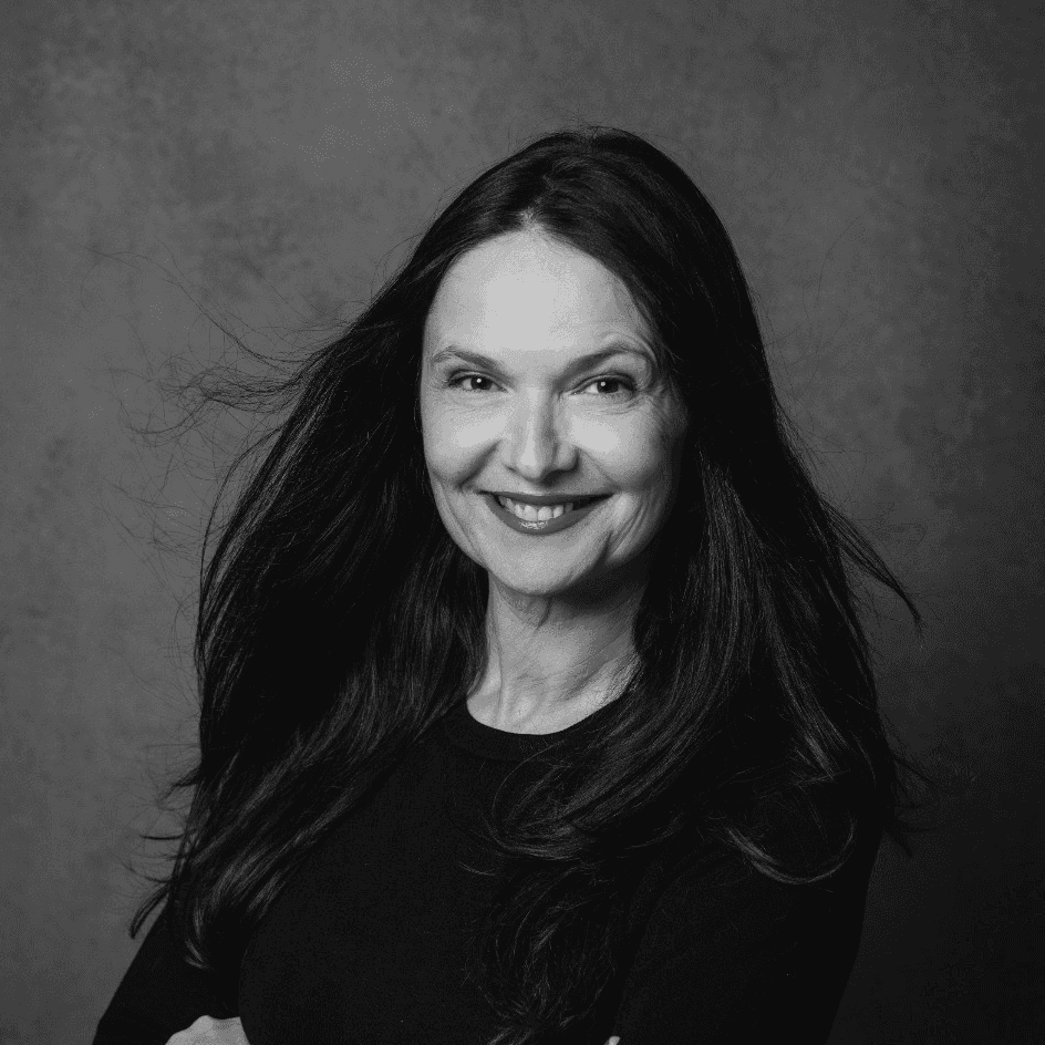 Porträt einer lächelnden Frau mit langen, fließenden Haaren und einem schwarzen Oberteil.