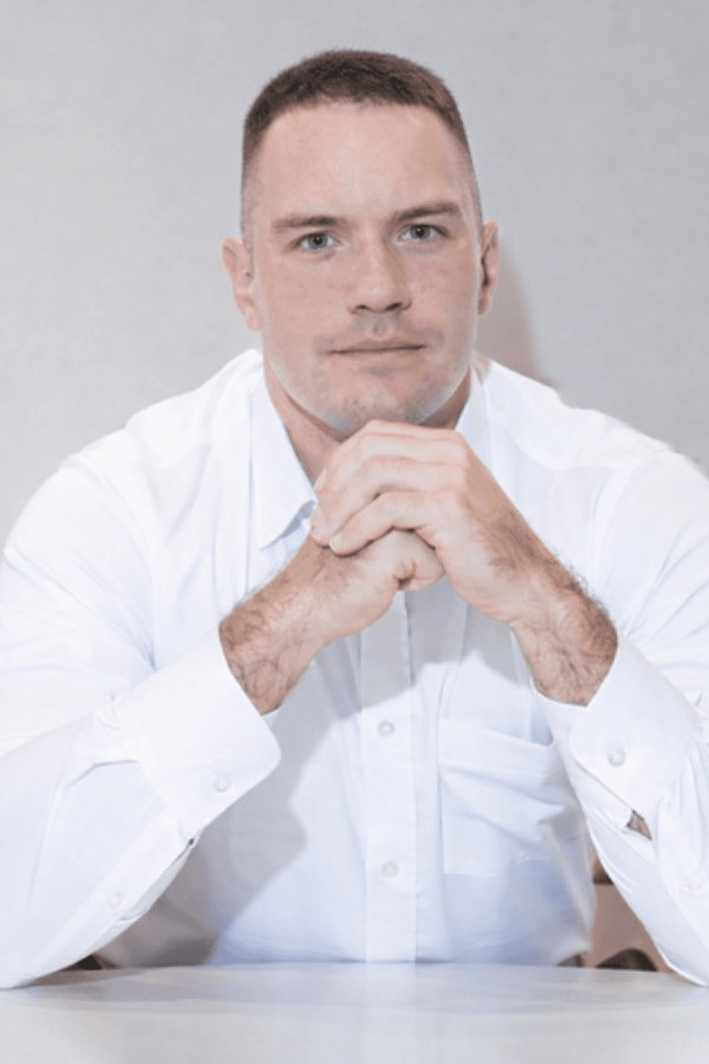 A young man in a white t-shirt stands against a light-colored background.