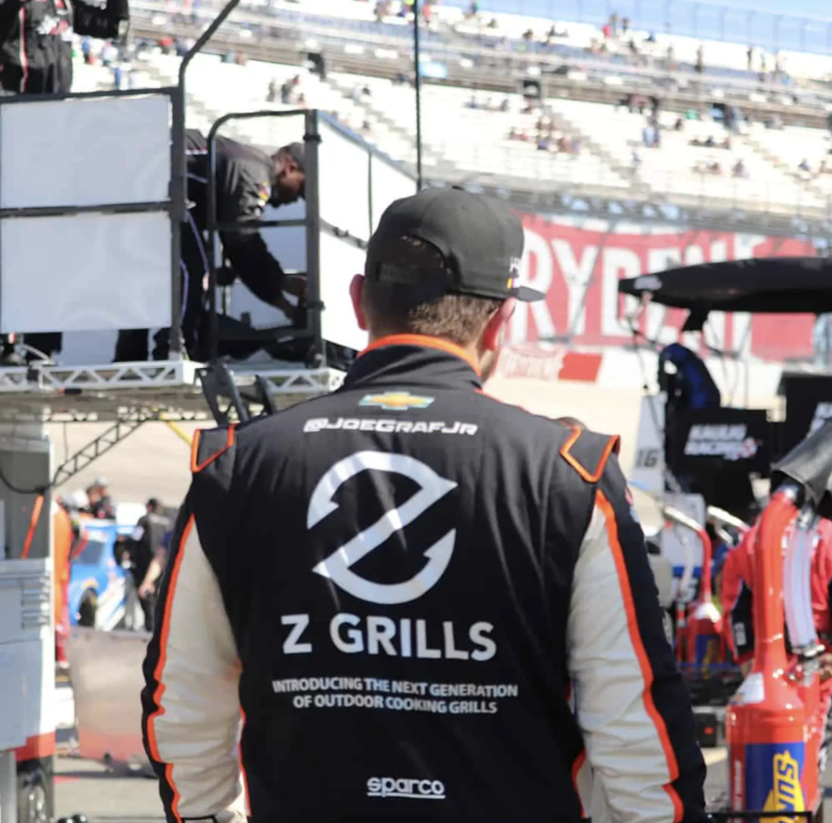 Joe Graf Jr in his racing suit with Z Grills branding on the back standing in the NASCAR pit area before a race.