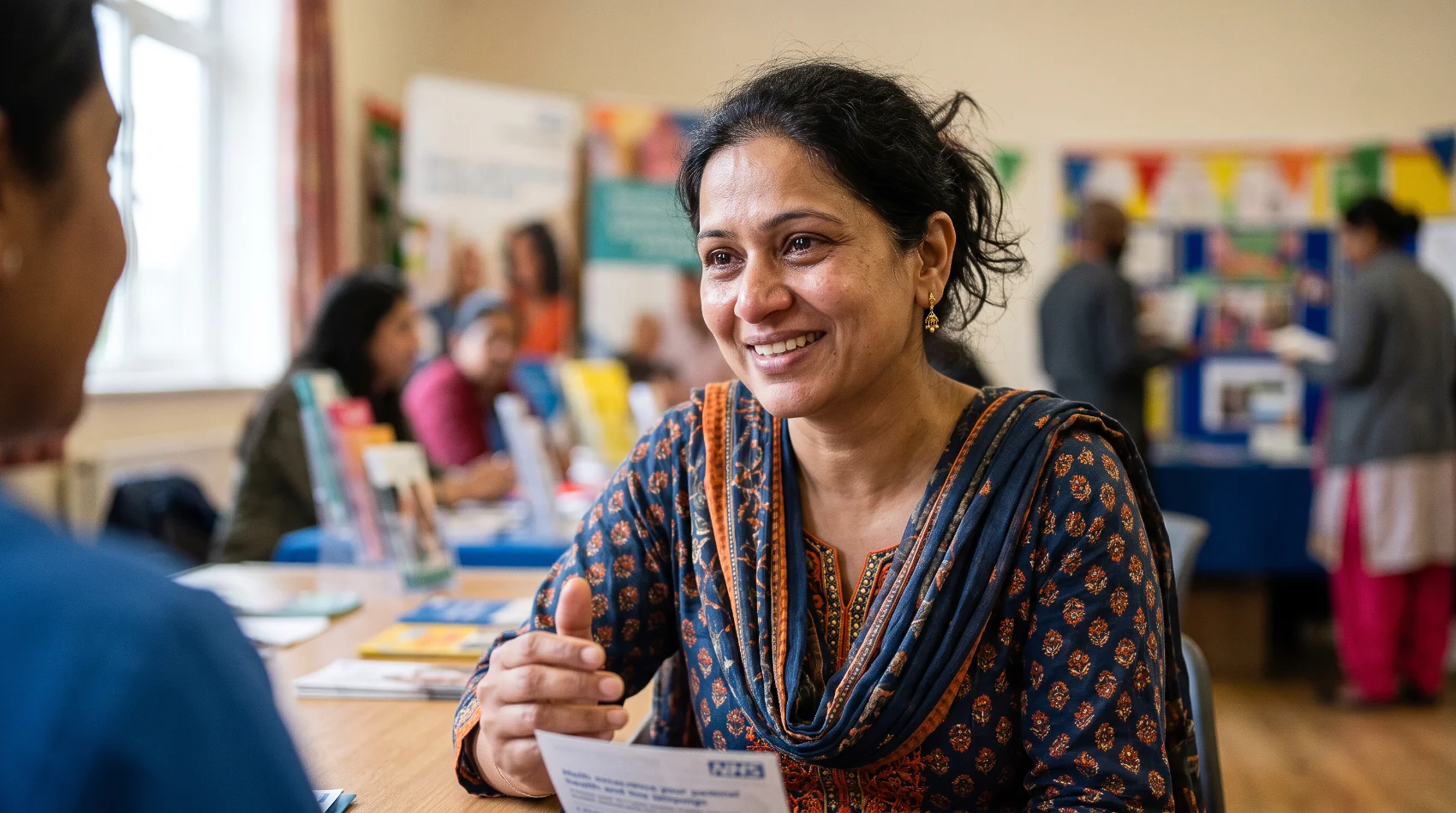 South Asian woman smiling receiving NHS hepatitis C awareness leaflet at community health event - Mediareach campaign