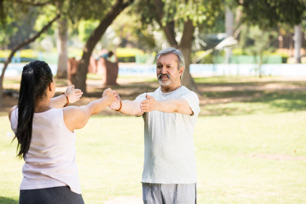 Senior man practicing guided stretching and mobility exercises with a physiotherapist outdoors.