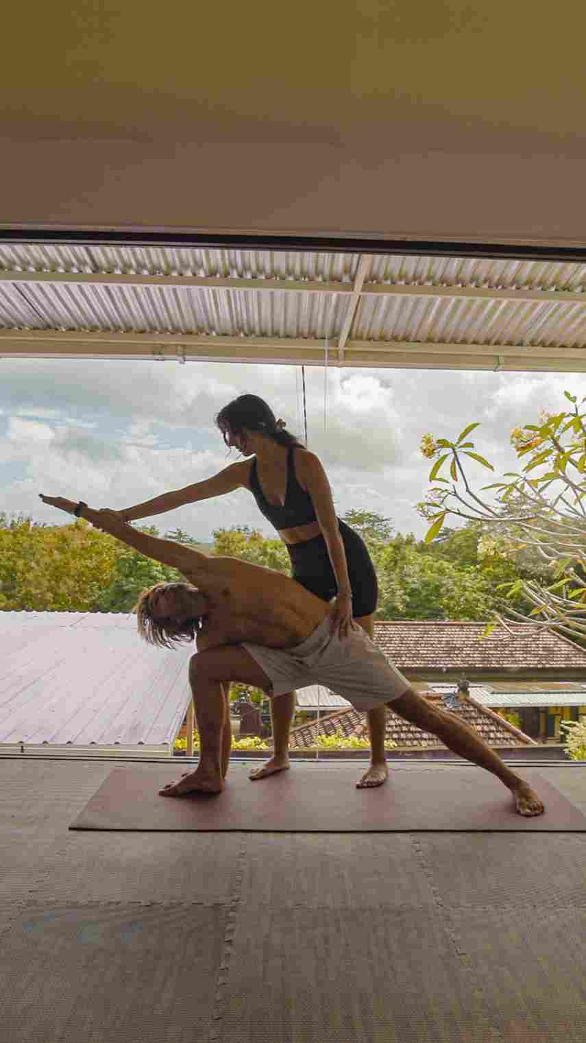 Yoga teacher providing hands-on adjustment for Extended Side Angle pose on the terrace at Ulu Yoga Bali.