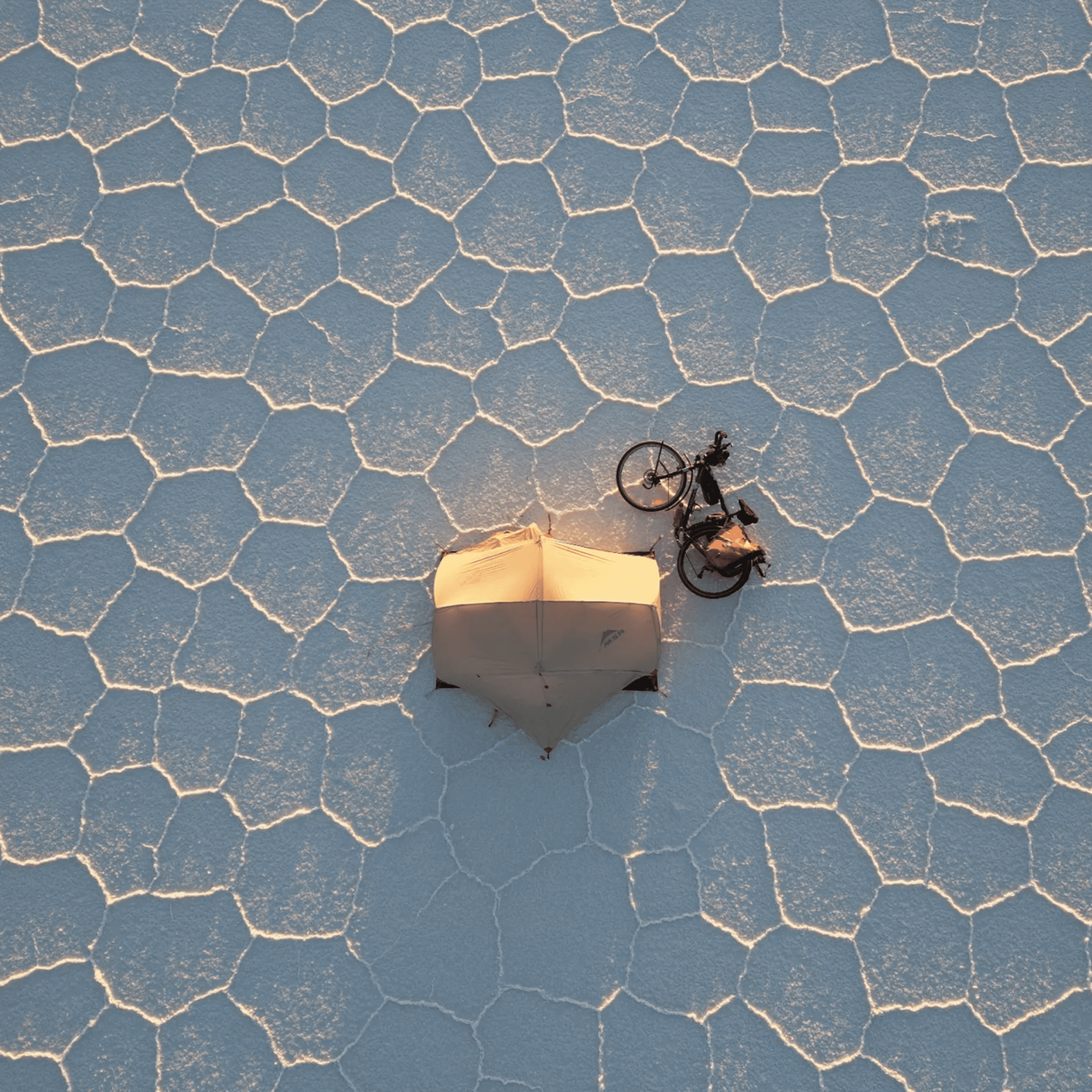 An overhead shot of a tent and a bike on the white hexagonal salt pans in Bolivia