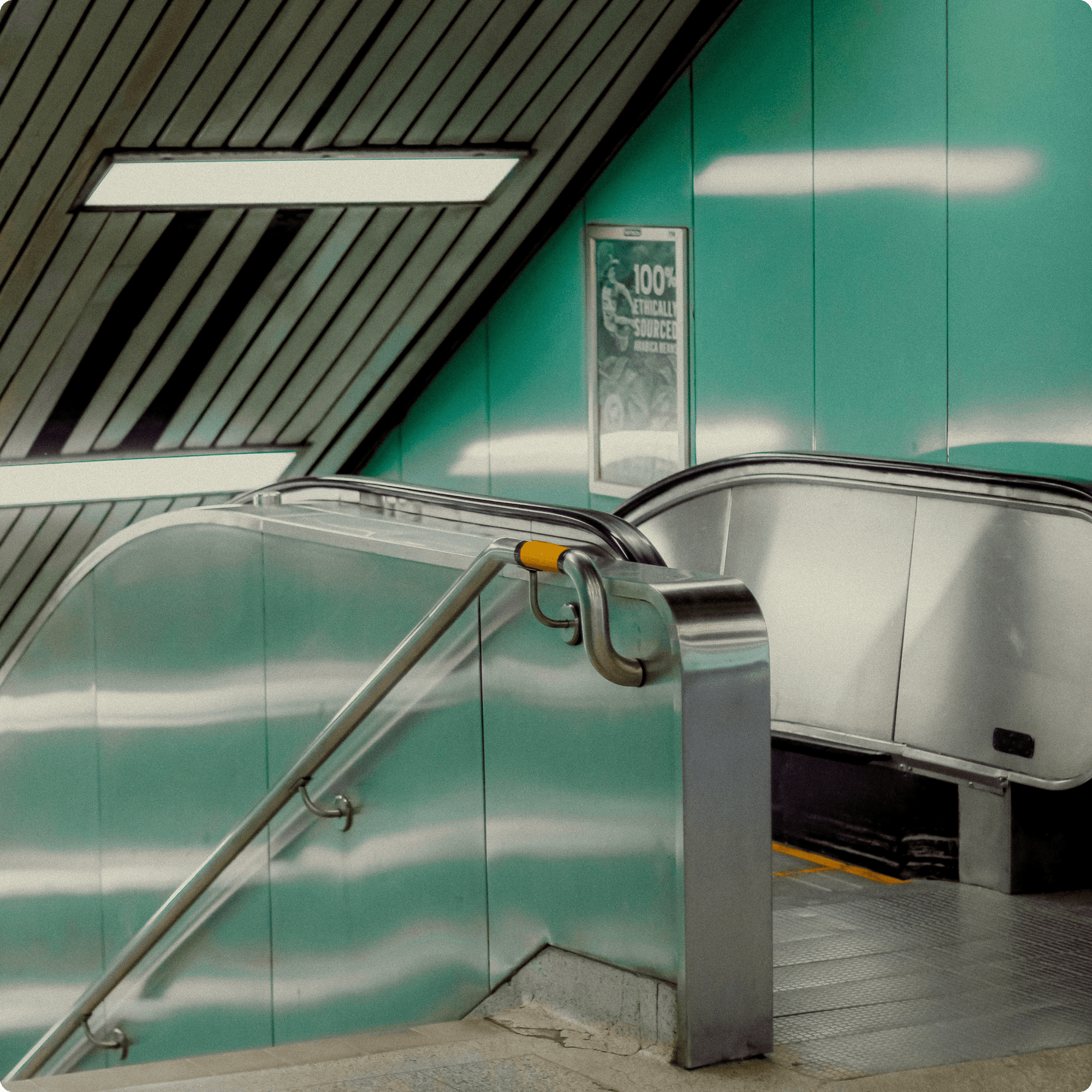 Modern metal escalator and stair railing in a transit station with teal walls