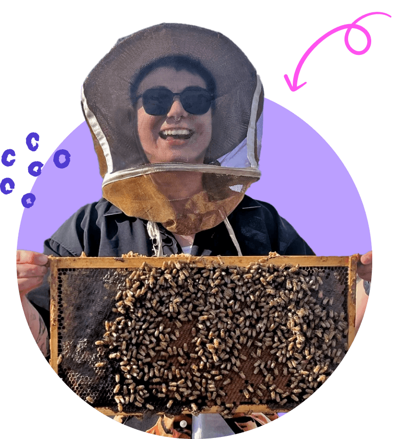 An image of Jo, grinning and holding a frame from a beehive loaded with honey bees.