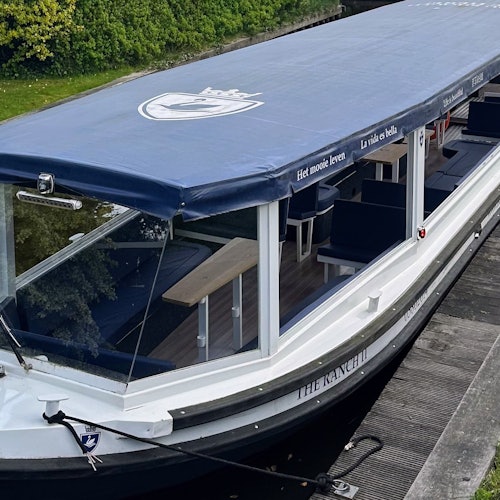 Sebuah perahu wisata tertutup berlabuh di samping kanal, dilengkapi dengan jendela kaca dan tempat duduk untuk penumpang.