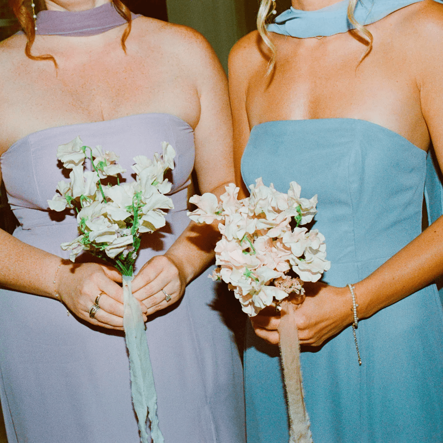 Two women in elegant dresses hold floral bouquets, showcasing their vibrant colors in a festive setting.