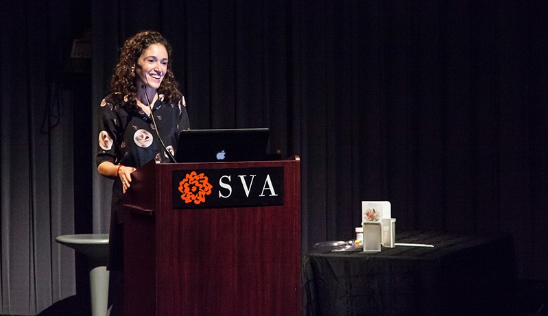 Portrait of a woman giving a speech from a wooden stand with the SVA logo on it