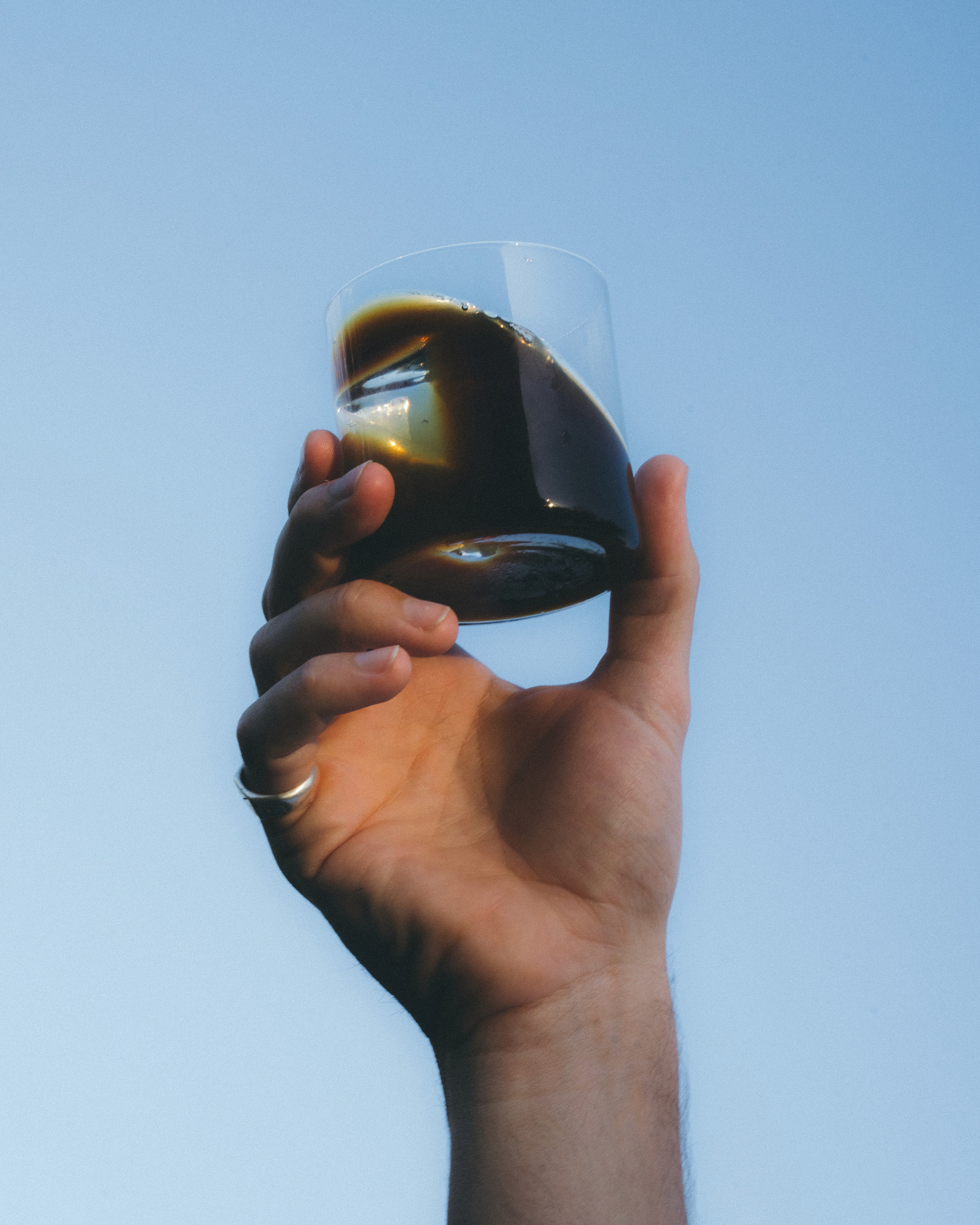 A splash of rich, dark coffee pours into a clear, elegant glass on a sleek blue surface, capturing the essence of a refreshing ice coffee experience.