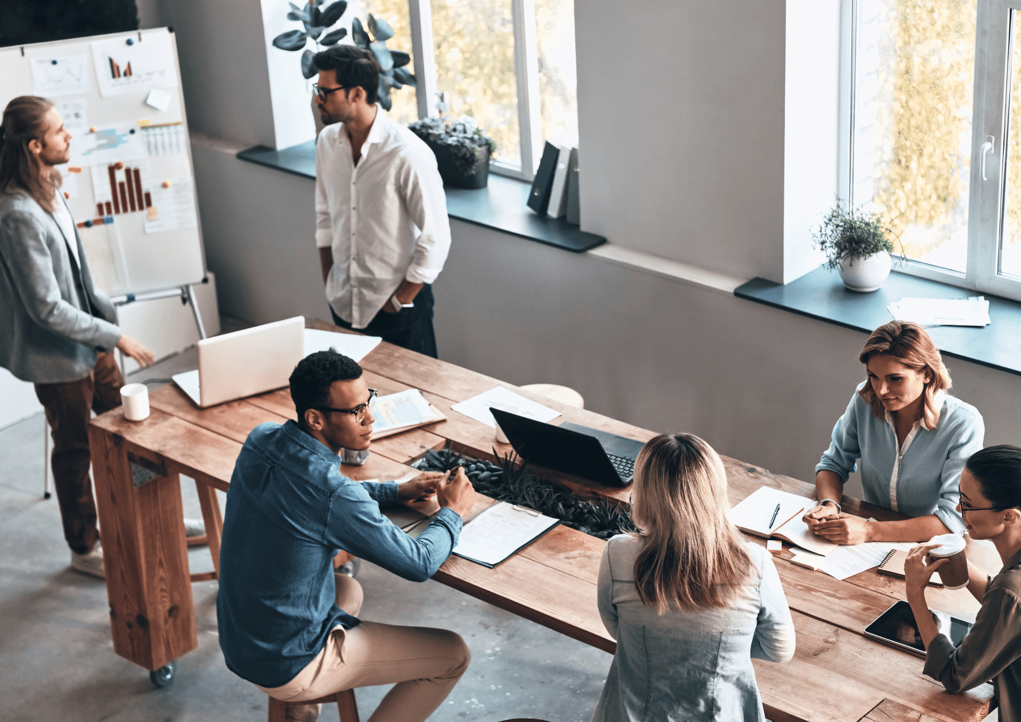 A team of professionals engages in a collaborative meeting around a shared workspace, fostering communication, strategy, and teamwork in a modern office.