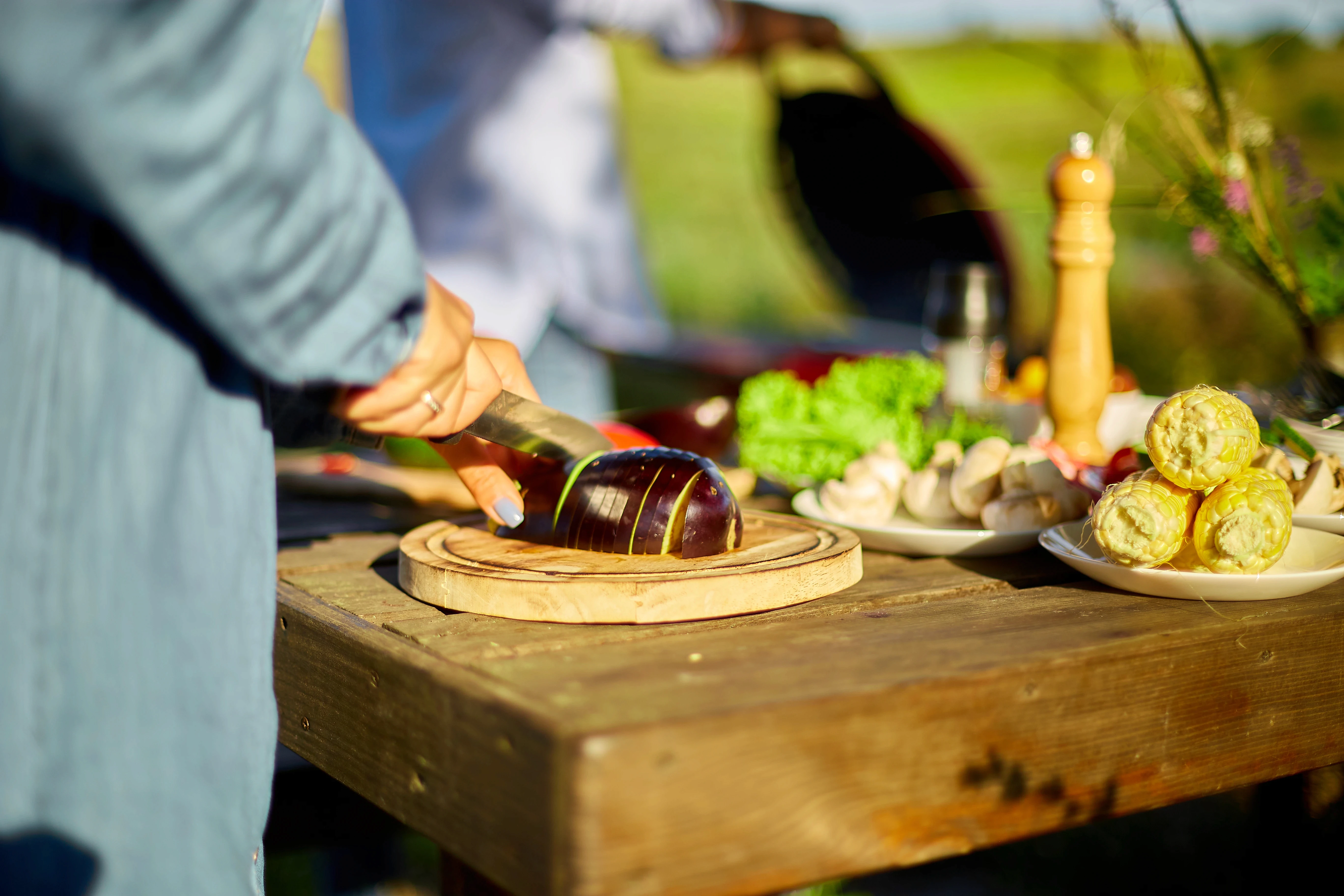 Close-up of a person slicing a fresh eggplant on a wooden table outdoors.