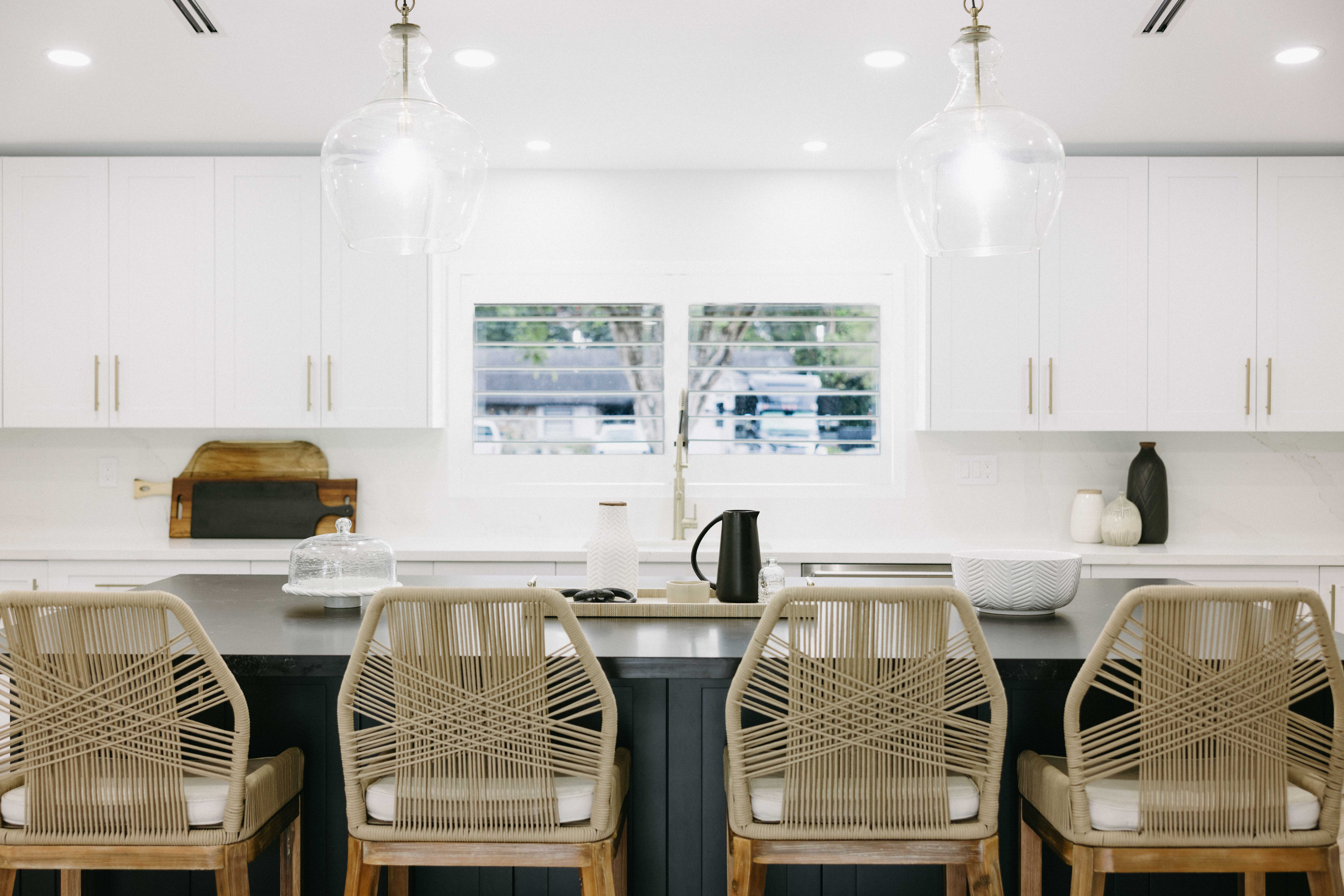 Modern kitchen island with four woven bar stools, white cabinets, and a window.