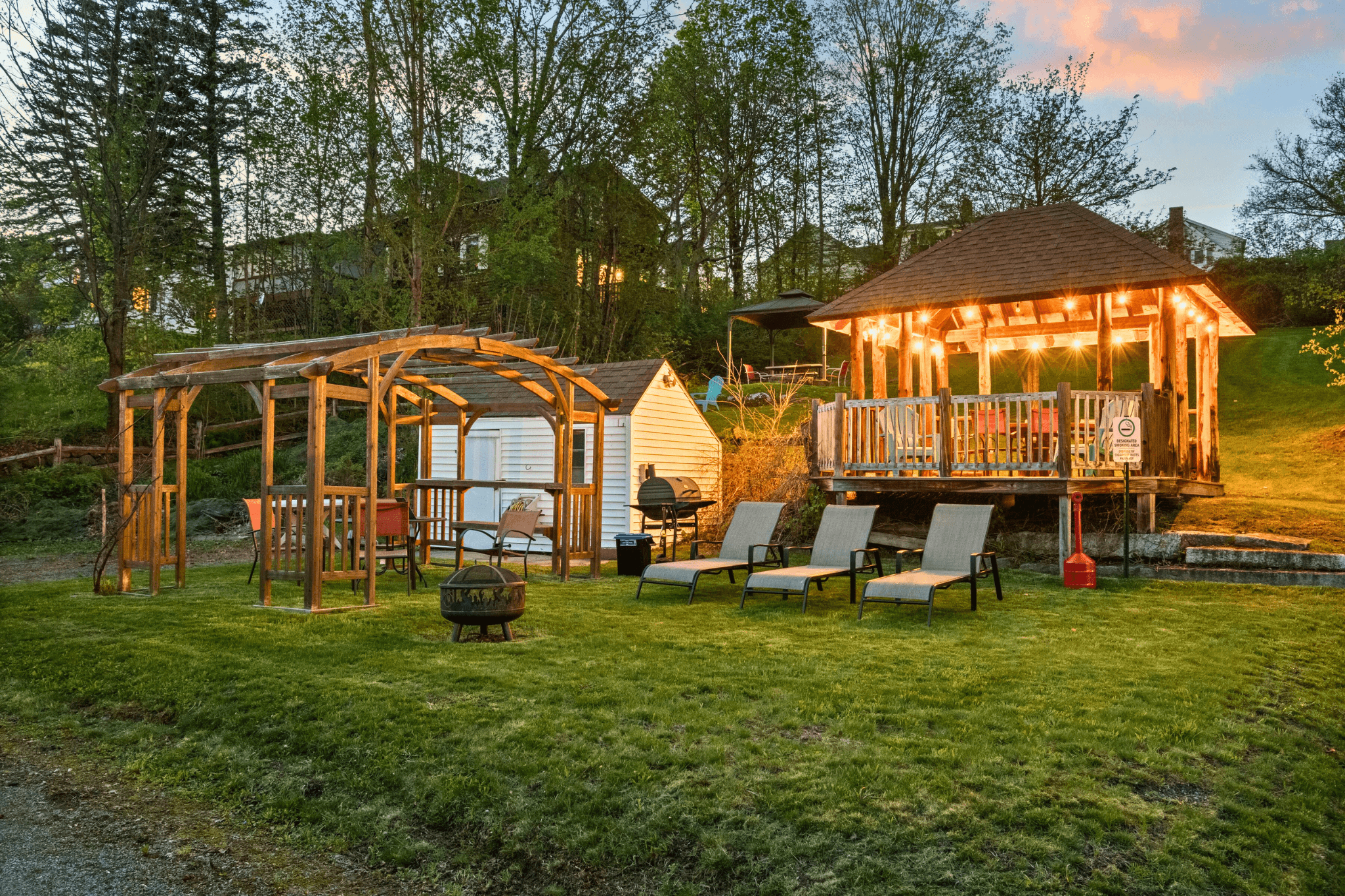 Cozy outdoor hangout space with a gazebo, firepit, and string lights surrounded by grassy lawn and mountain views—perfect for socializing at this small-town New Hampshire short-term rental.